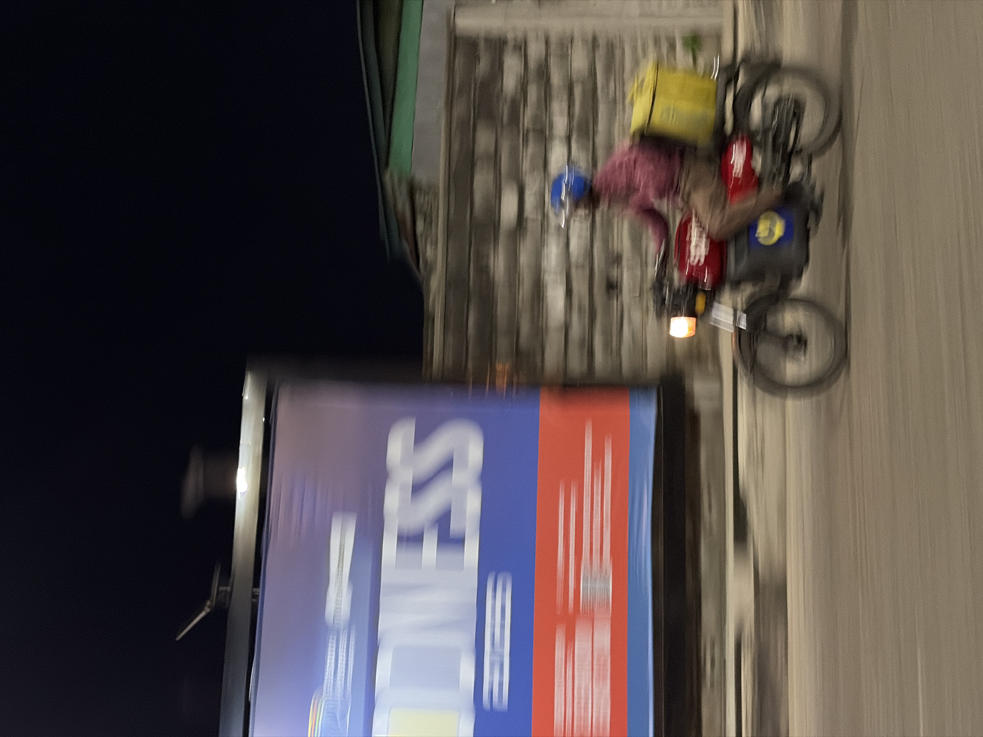 Delivery rider passes billboard on Itirin street at night