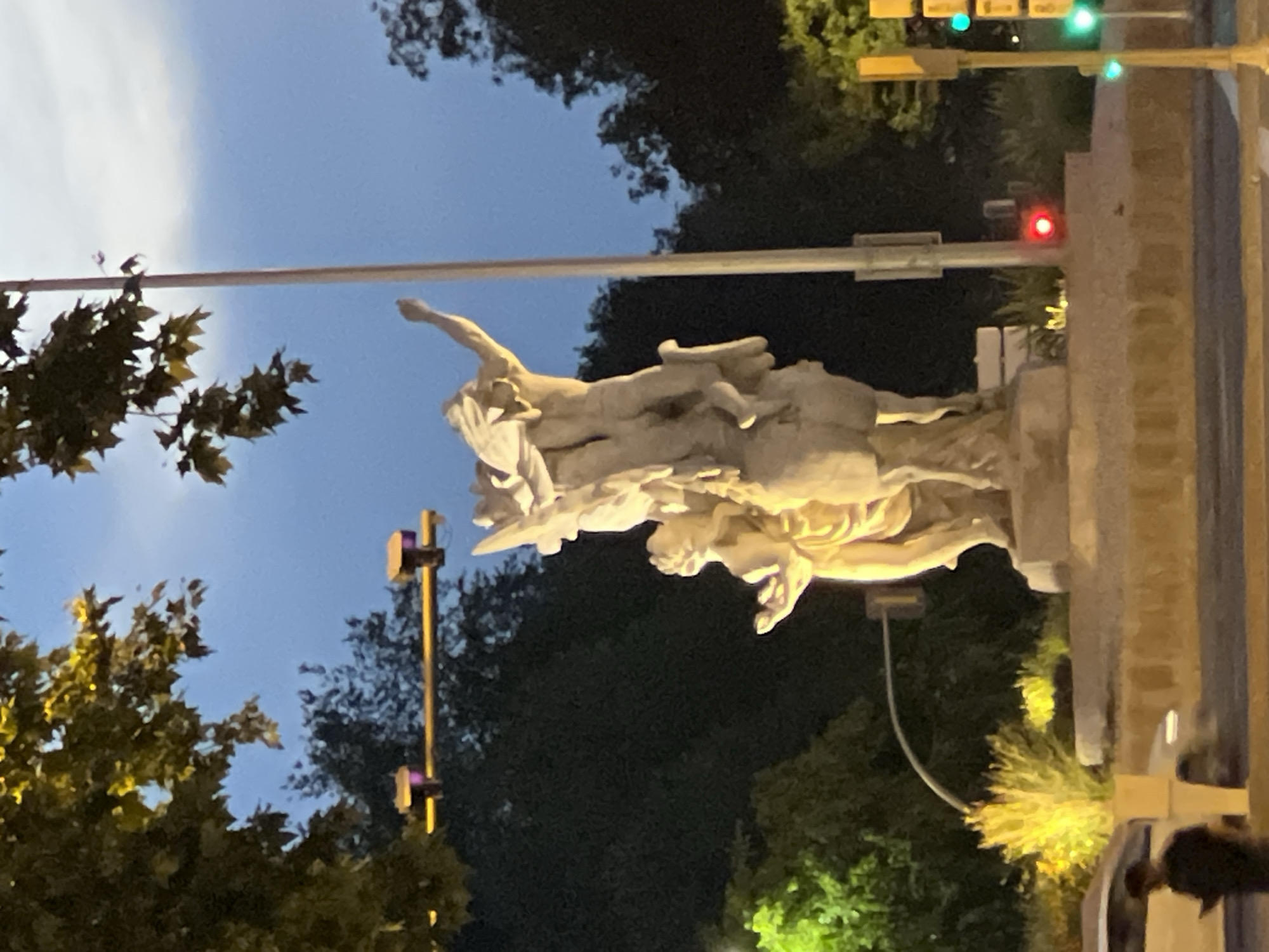 Evening streetlights illuminate three-figure stone sculpture in Madrid