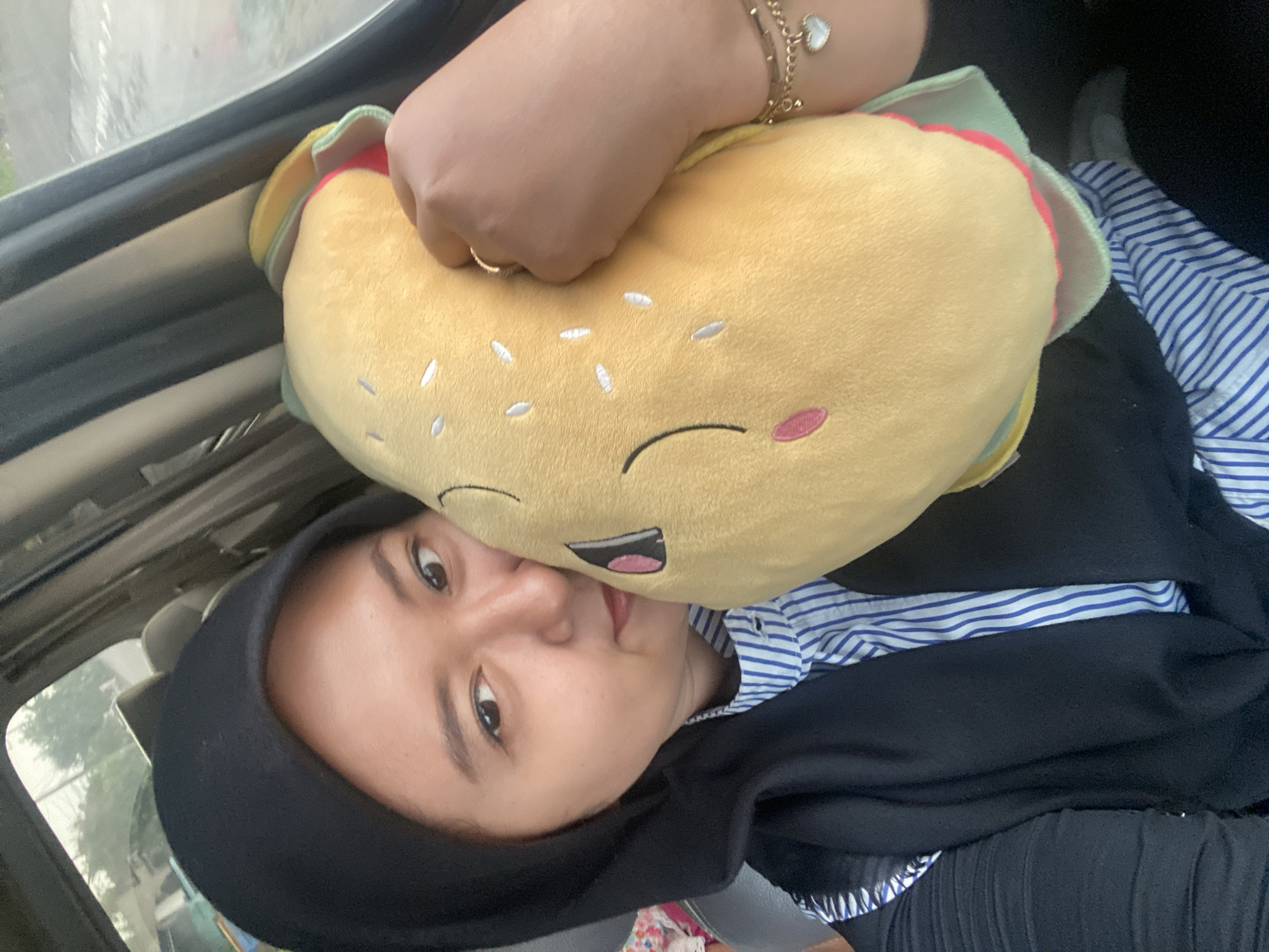 Woman holds burger plush toy in vehicle in Tlasih
