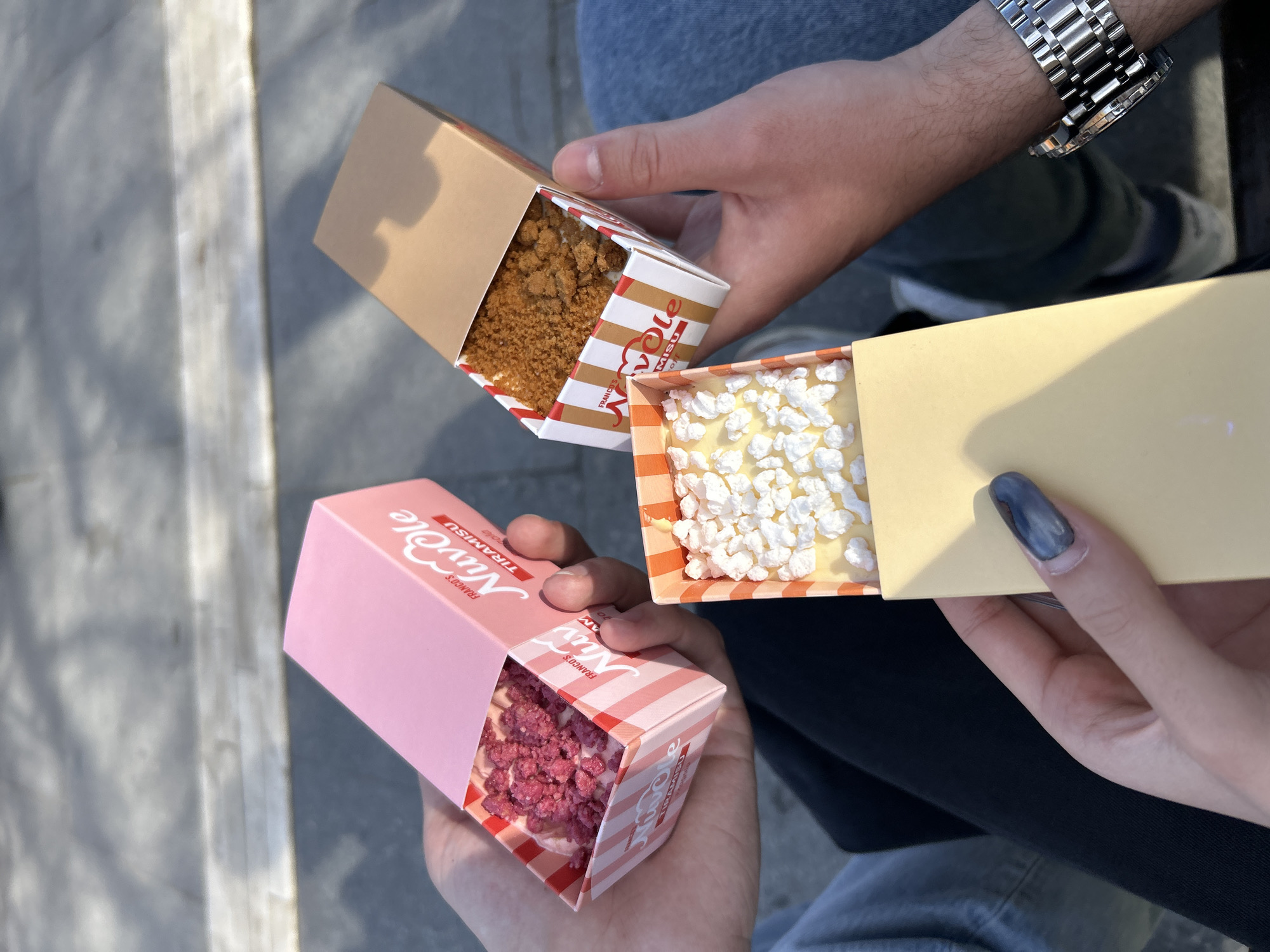 Three people enjoy tiramisu boxes near Sofia's NDK building
