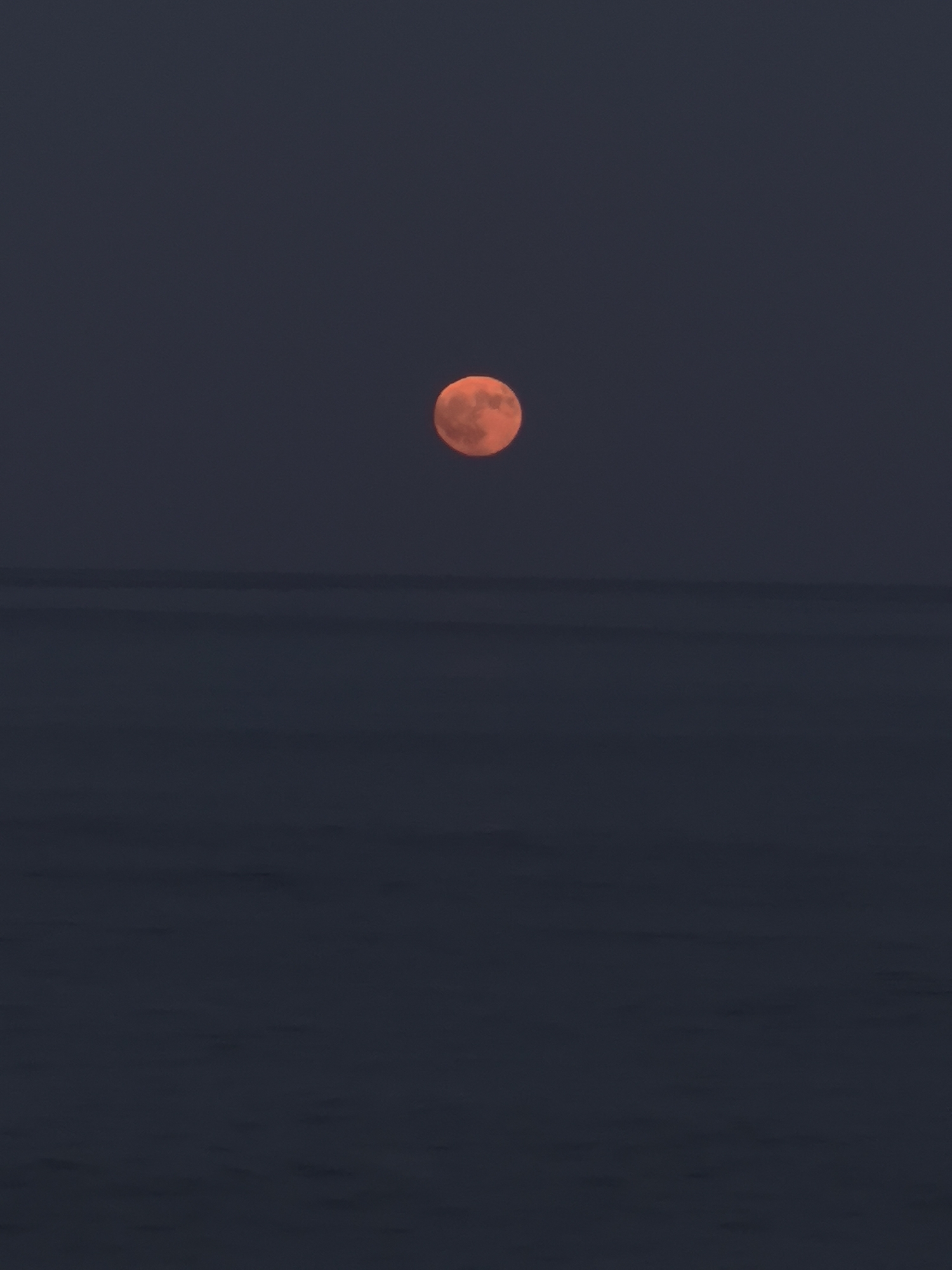 Orange moon rises over a calm Golden Beach at dusk