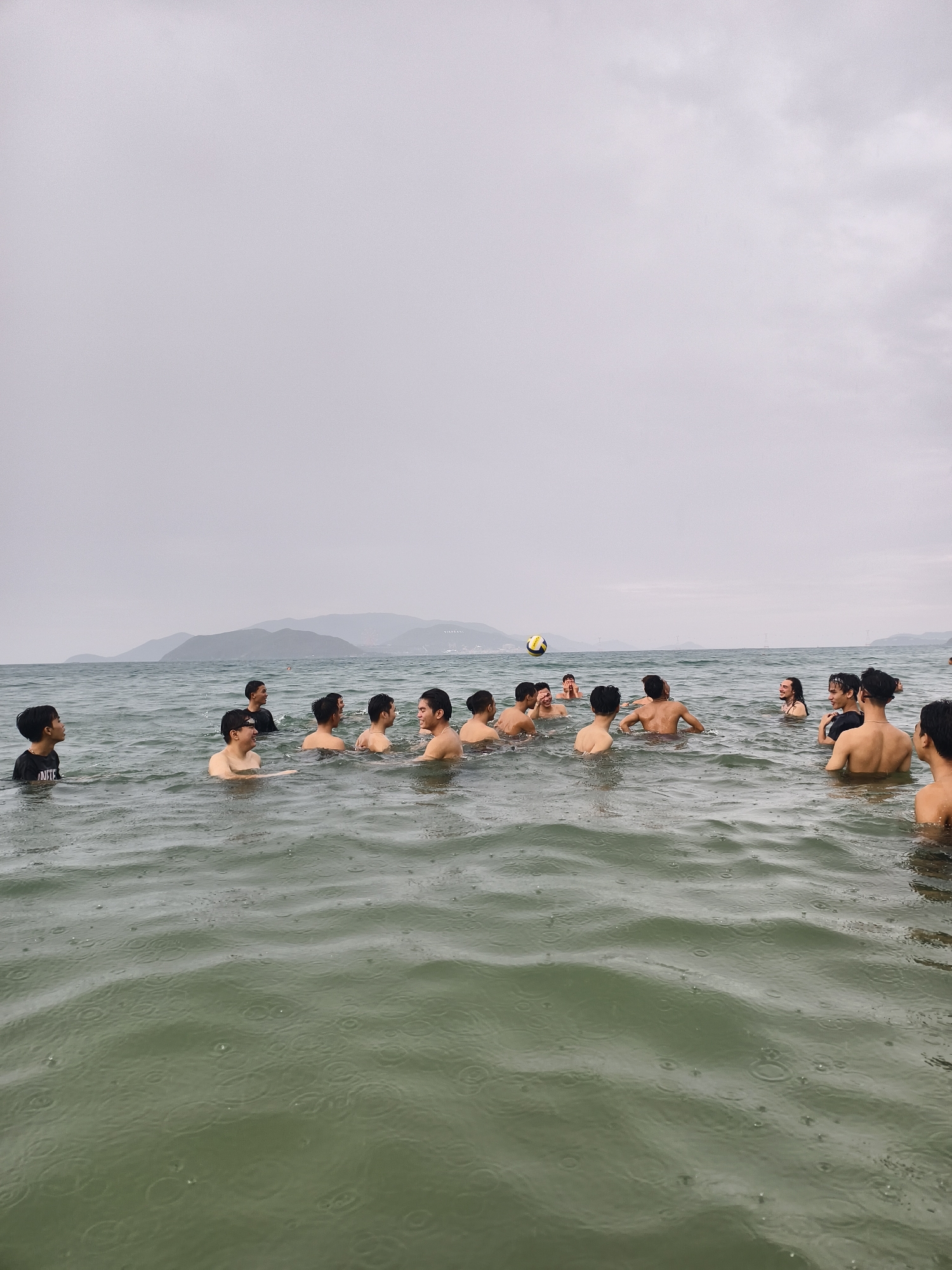 Young men play water volleyball at crowded beach