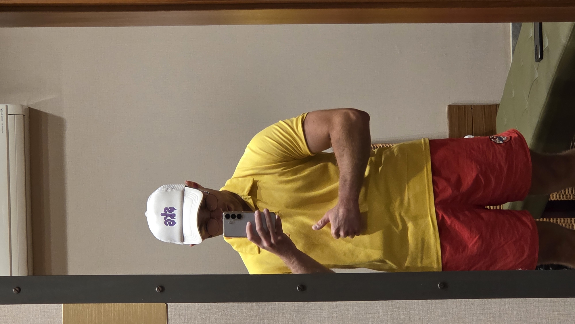 Mirror selfies in a bold yellow polo and purple-lettered hat