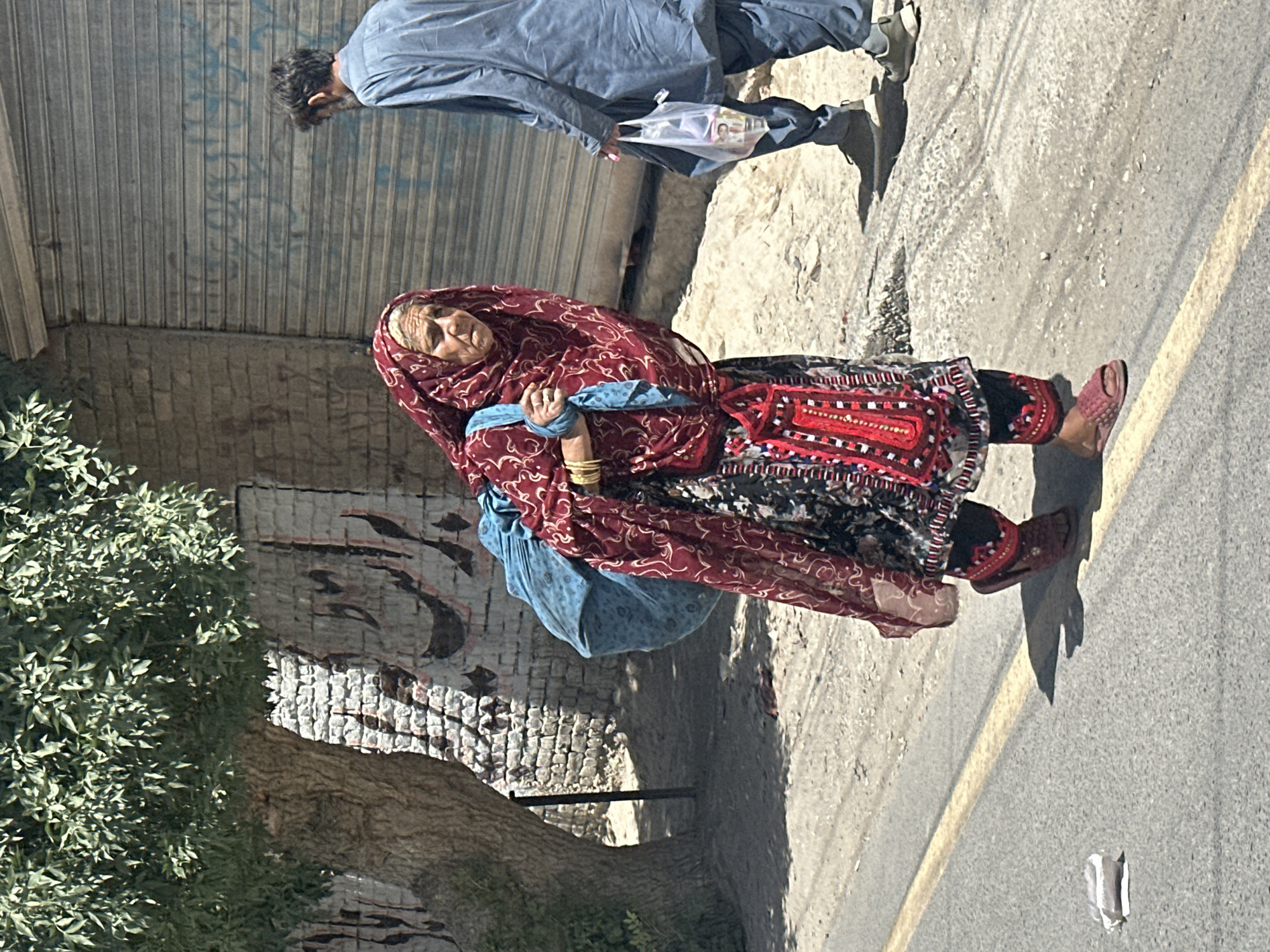 Elderly woman in traditional dress walks Quetta street