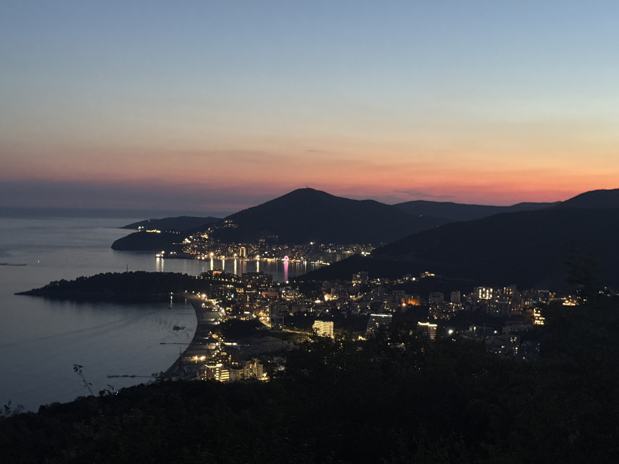 Coastal city glows under a twilight sky from above