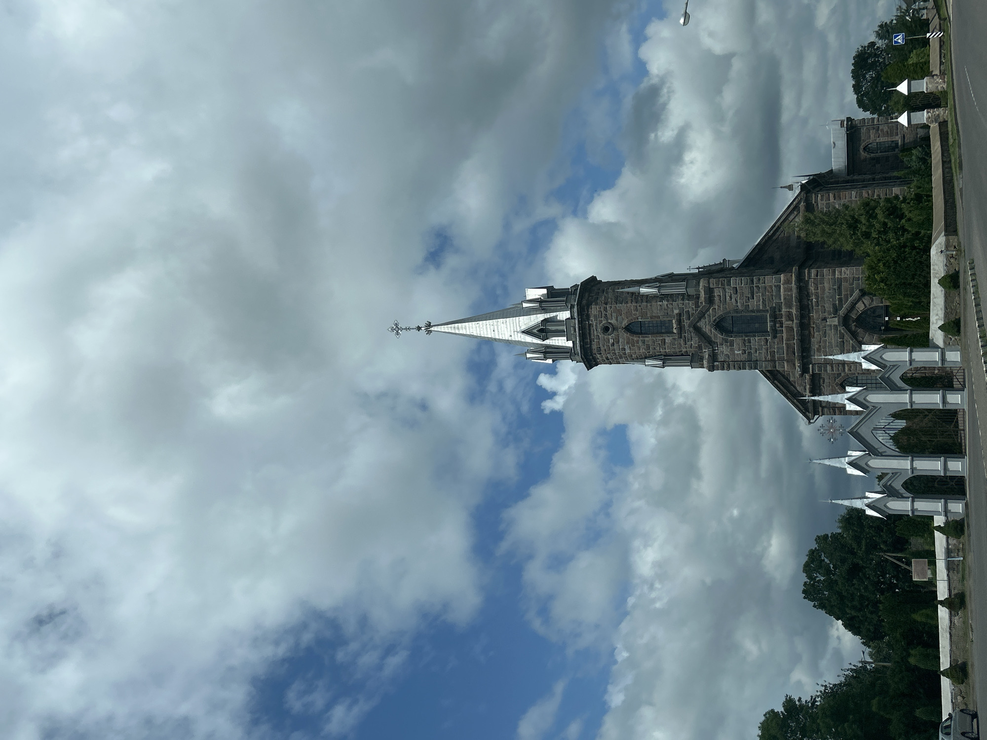 Stone church with pointed spire behind ornate gates, rural Belarus