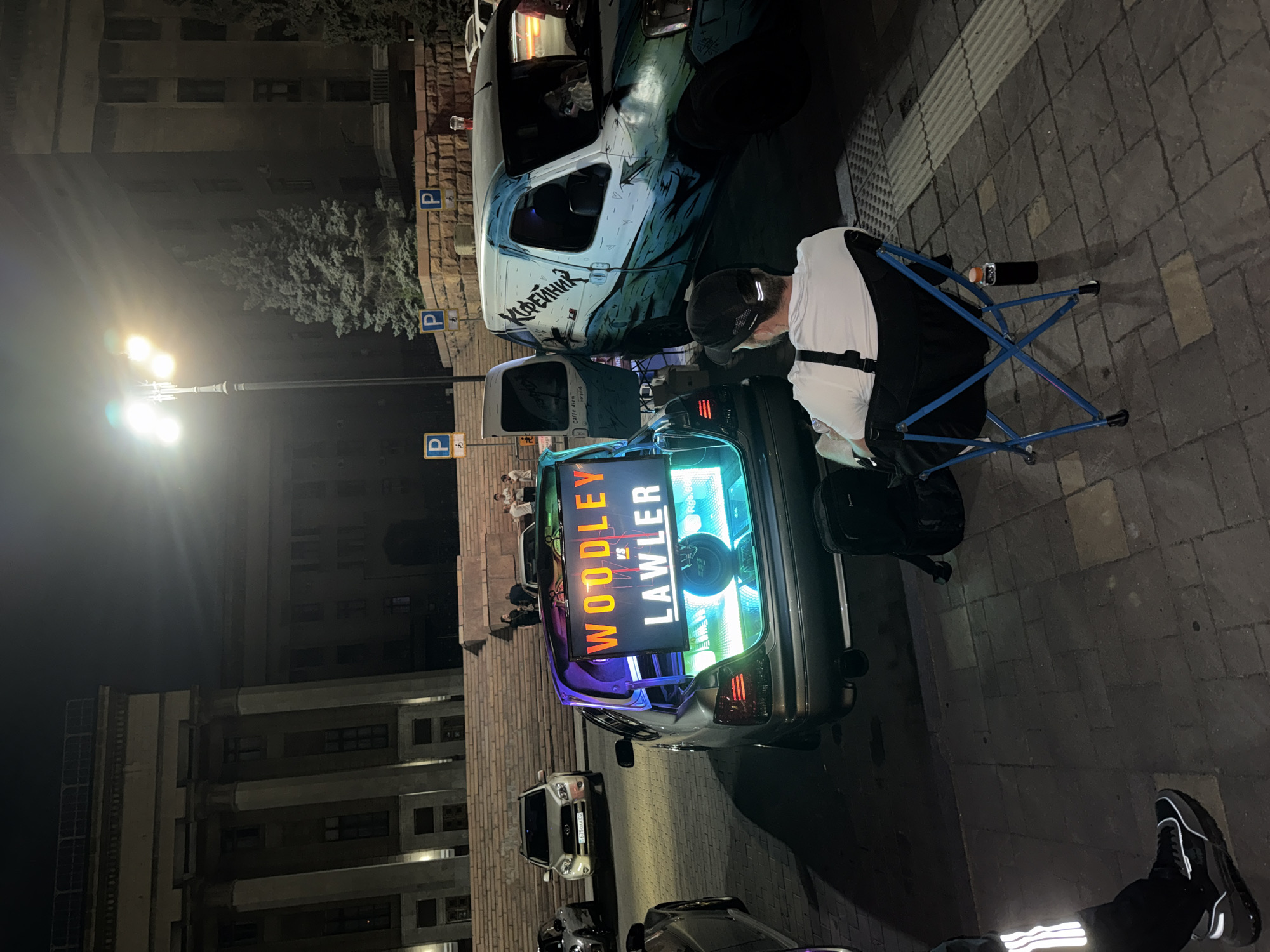 Late-night square hangout with dogs, coffee, and a trunk gaming setup