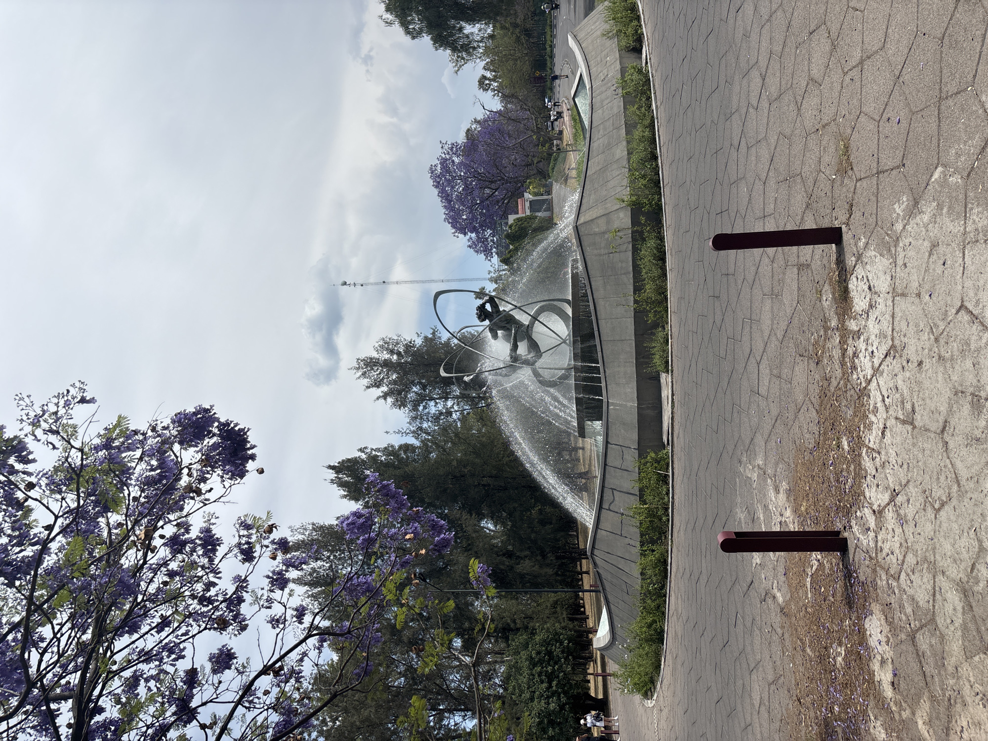 Orbital sculpture fountain spotted amid purple-flowered trees in Mexico City