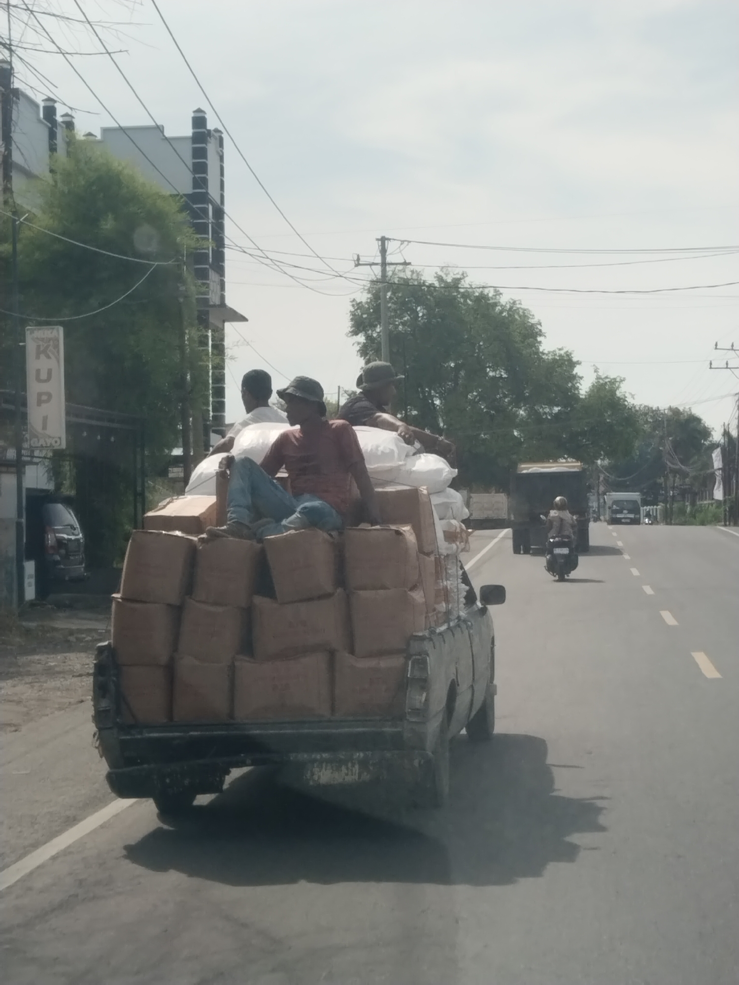 Loaded truck carries three passengers atop cargo in Indonesia