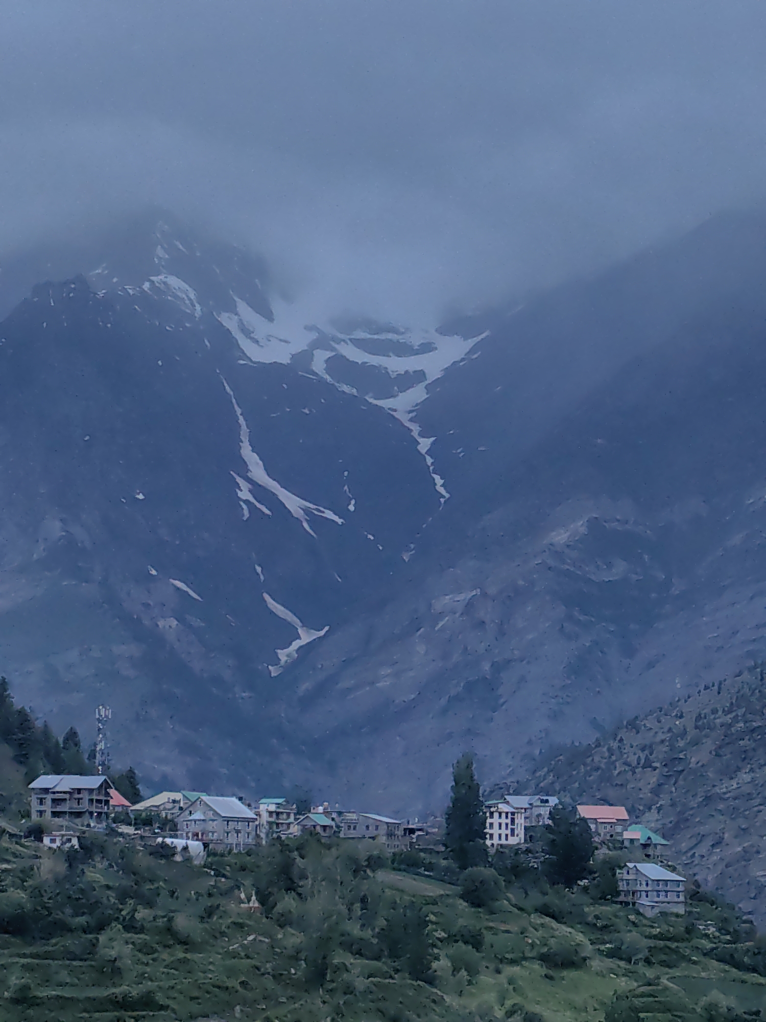Keylong village under cloudy skies, prayer flags and snowy peaks