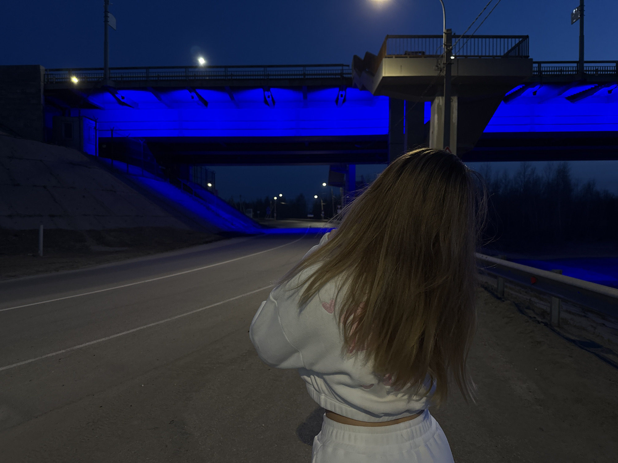 Person observes blue-illuminated bridge at night in April 2026