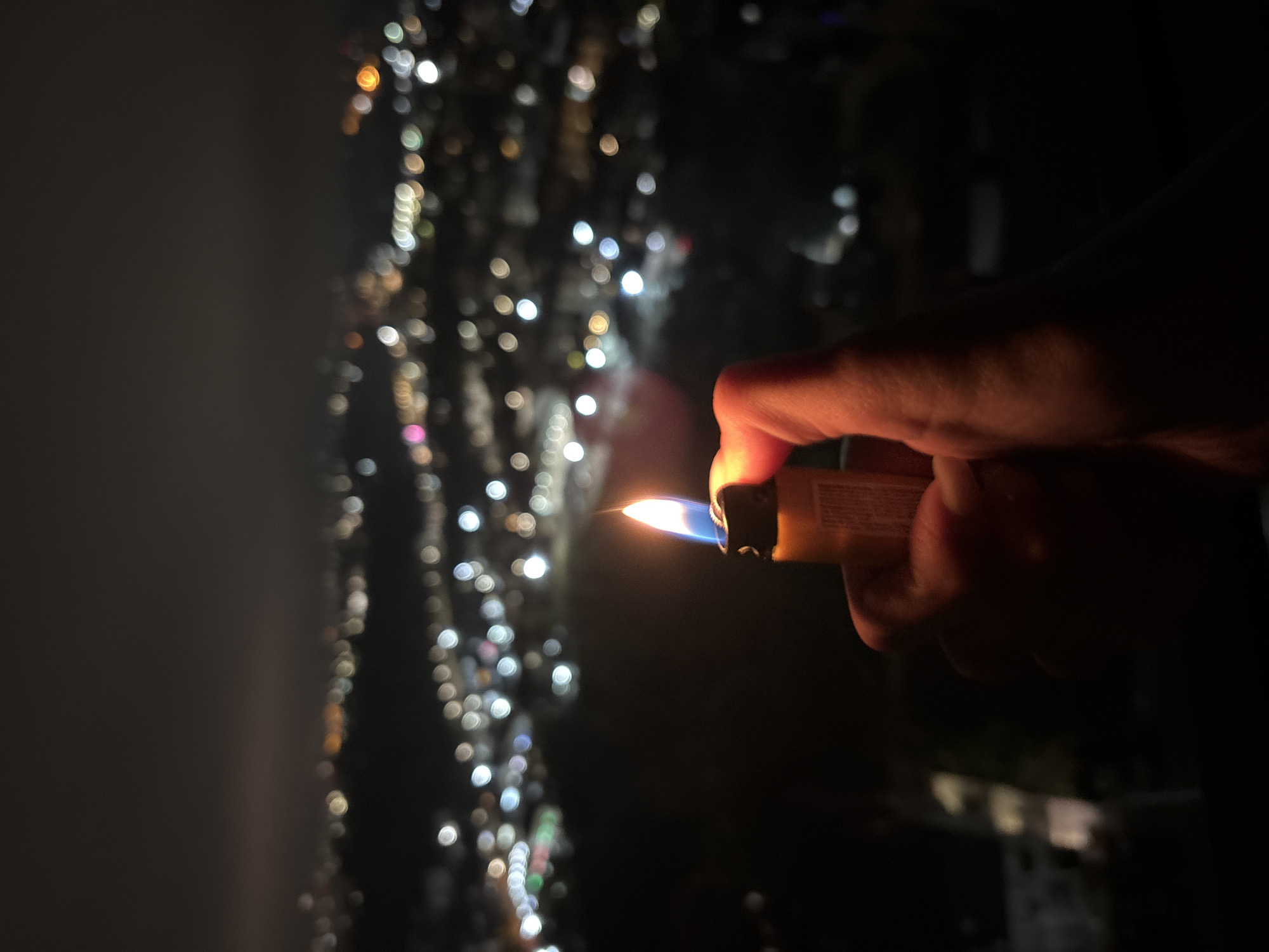 Person holds lit lighter against city lights in Sochi