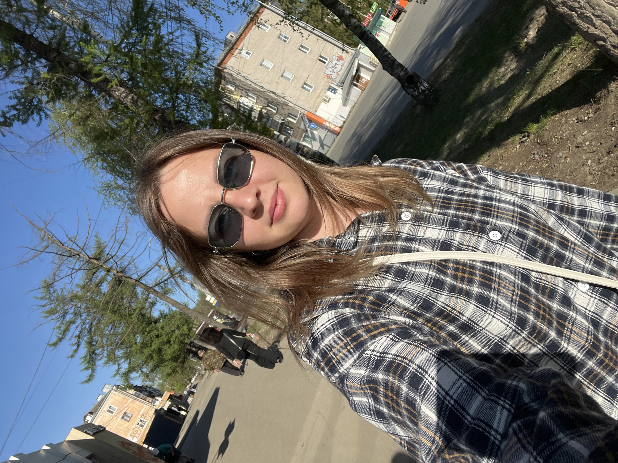 Woman takes selfie on tree-lined street in Izhevsk