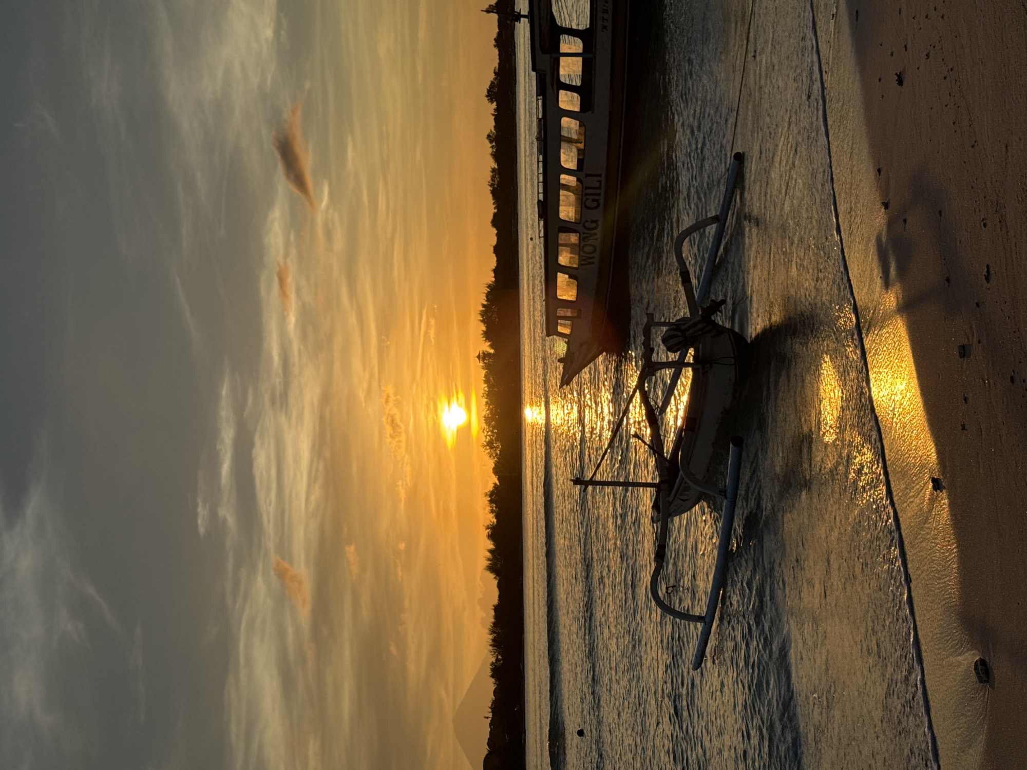 Indonesian beach sunset captured with traditional boats and tourist selfies