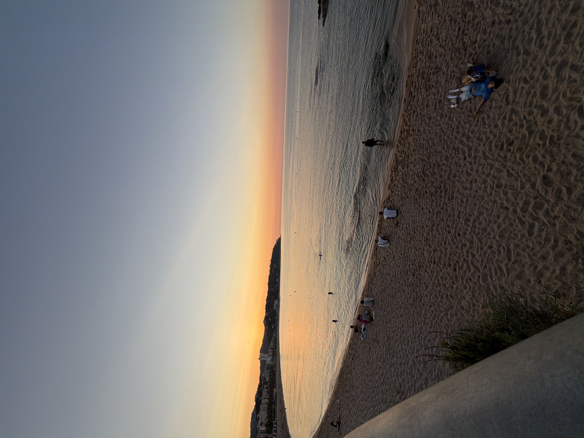 Calm beach at sunset with rocky coastline and scattered figures