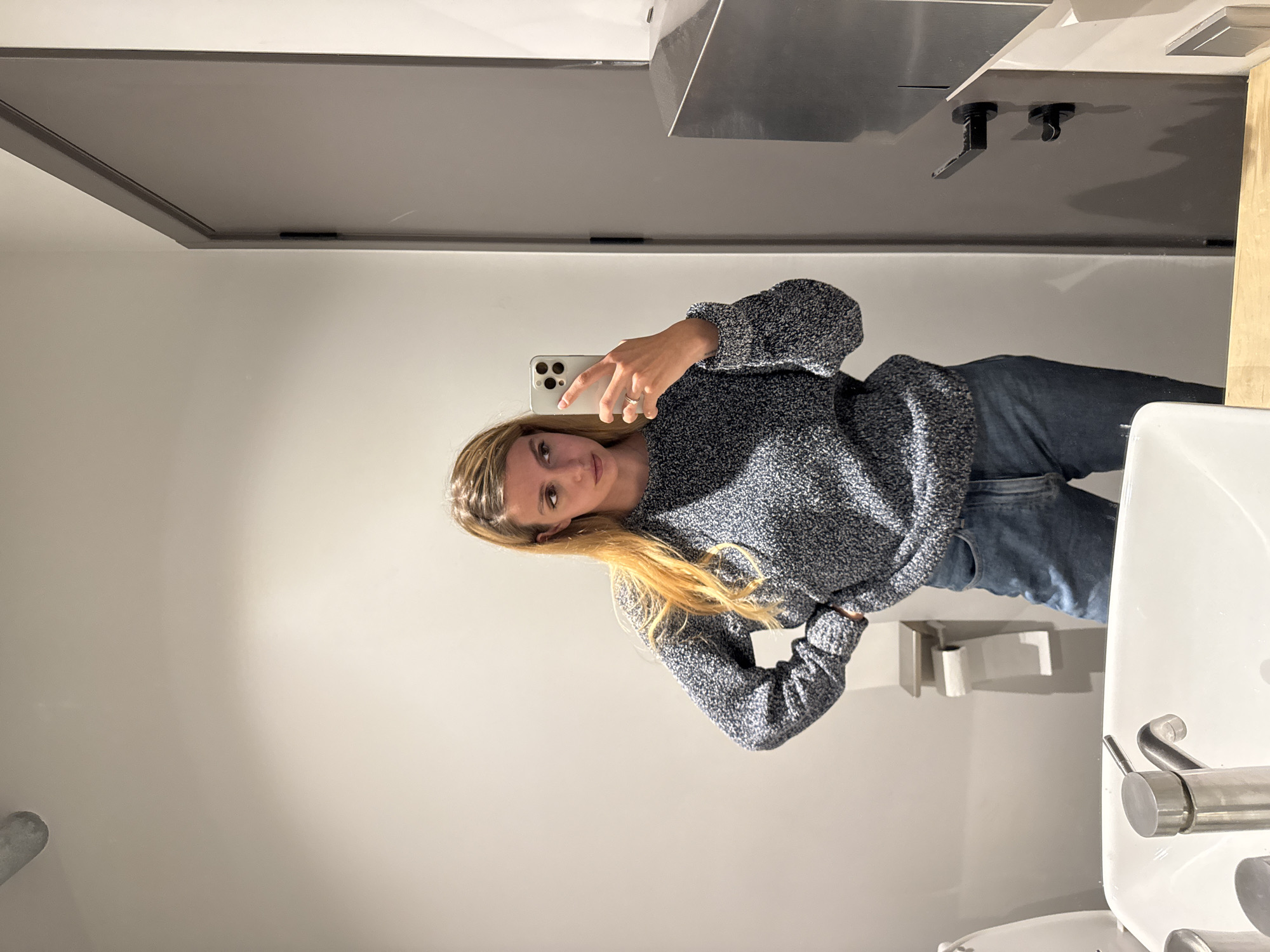 Woman takes bathroom mirror selfies in blue sweater