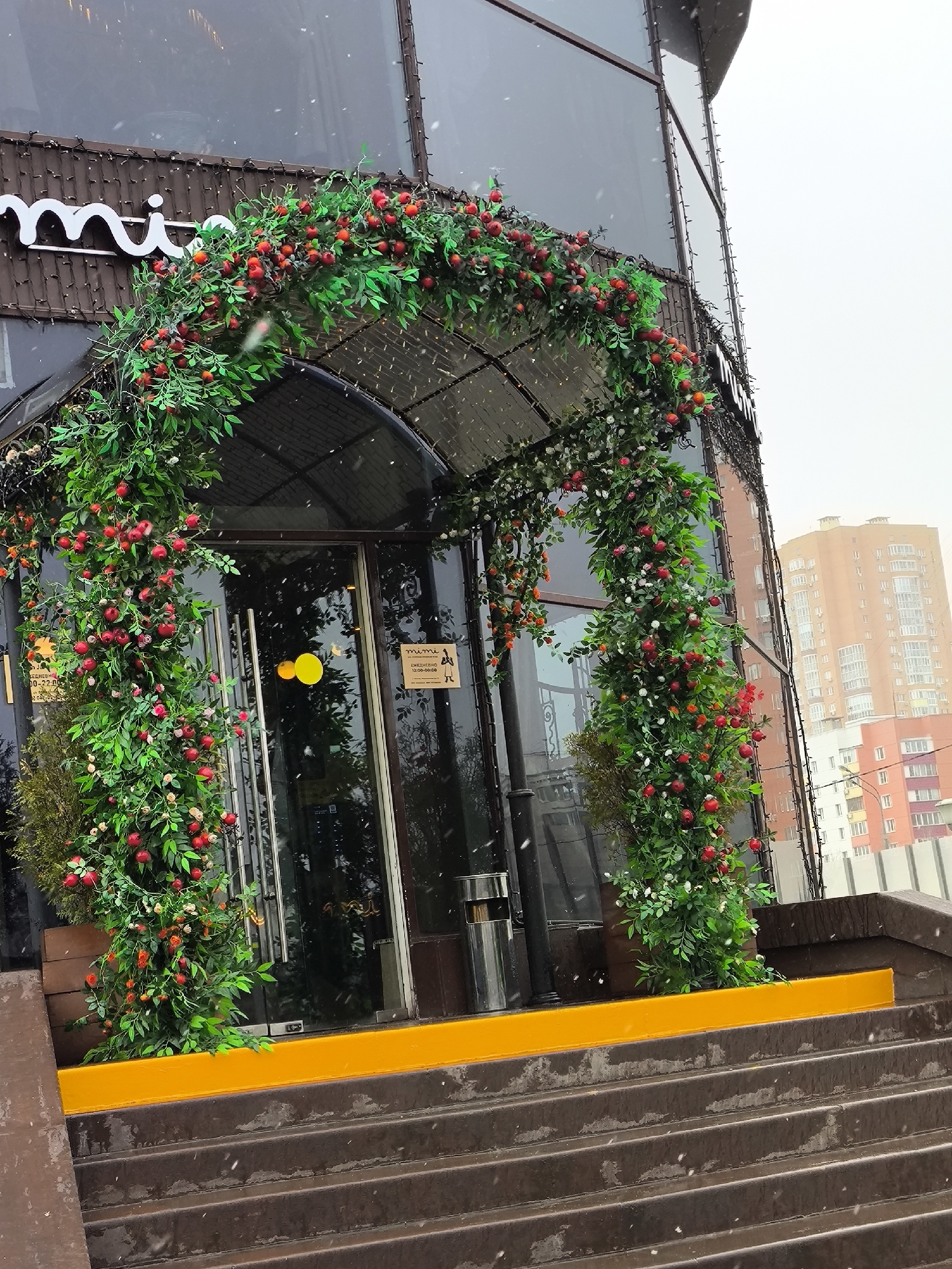 Commercial building entrance with decorative greenery archway documented