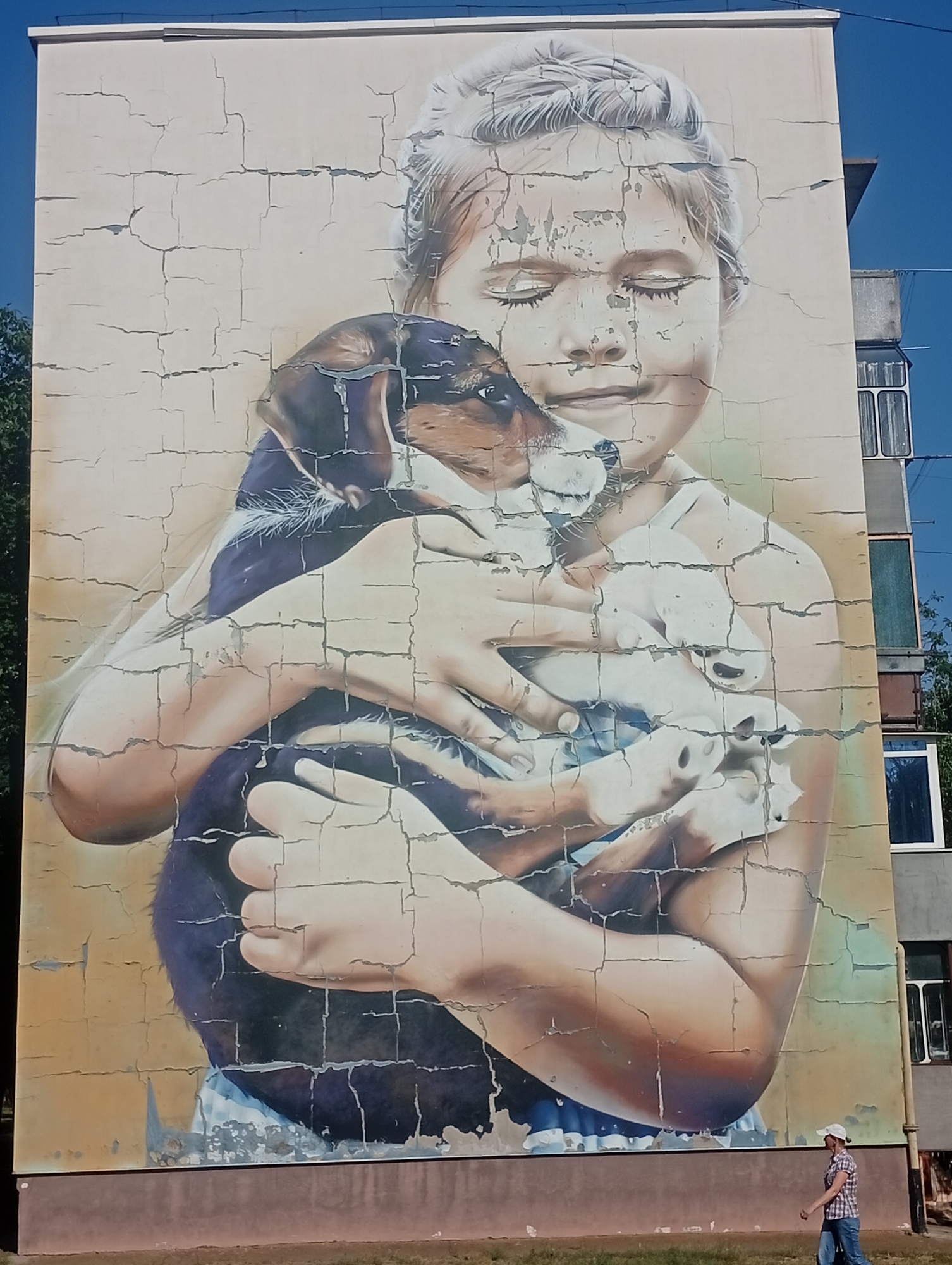 Weathered mural in Pokrov depicts a figure holding a puppy