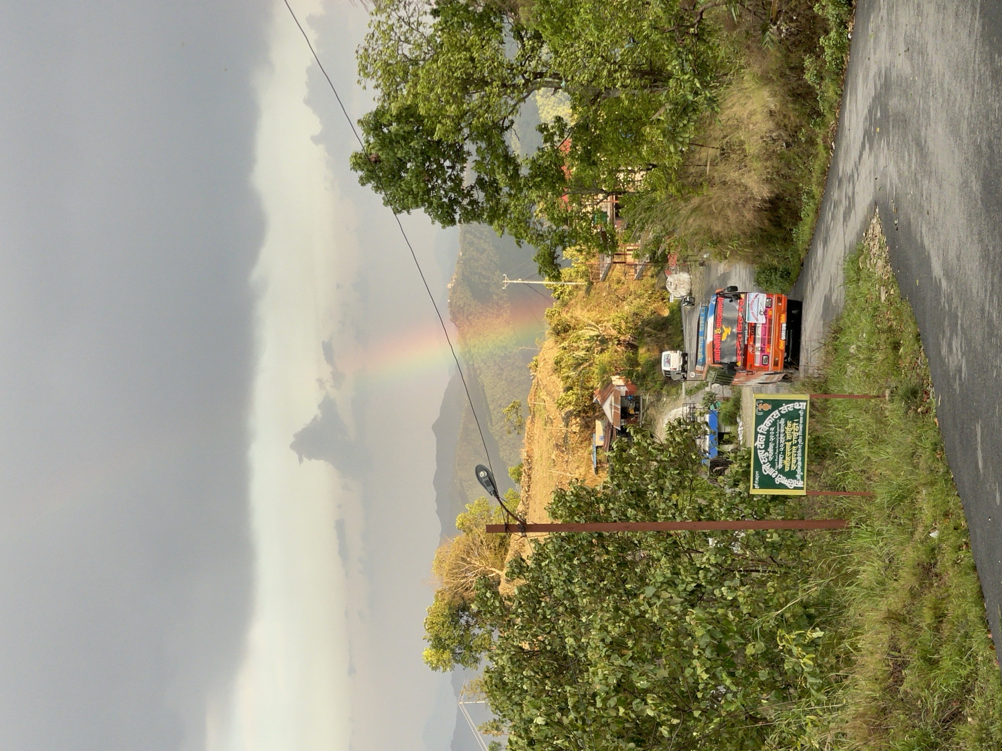Rainbow arcs over Pokhara mountains amid cloudy Nepal skies