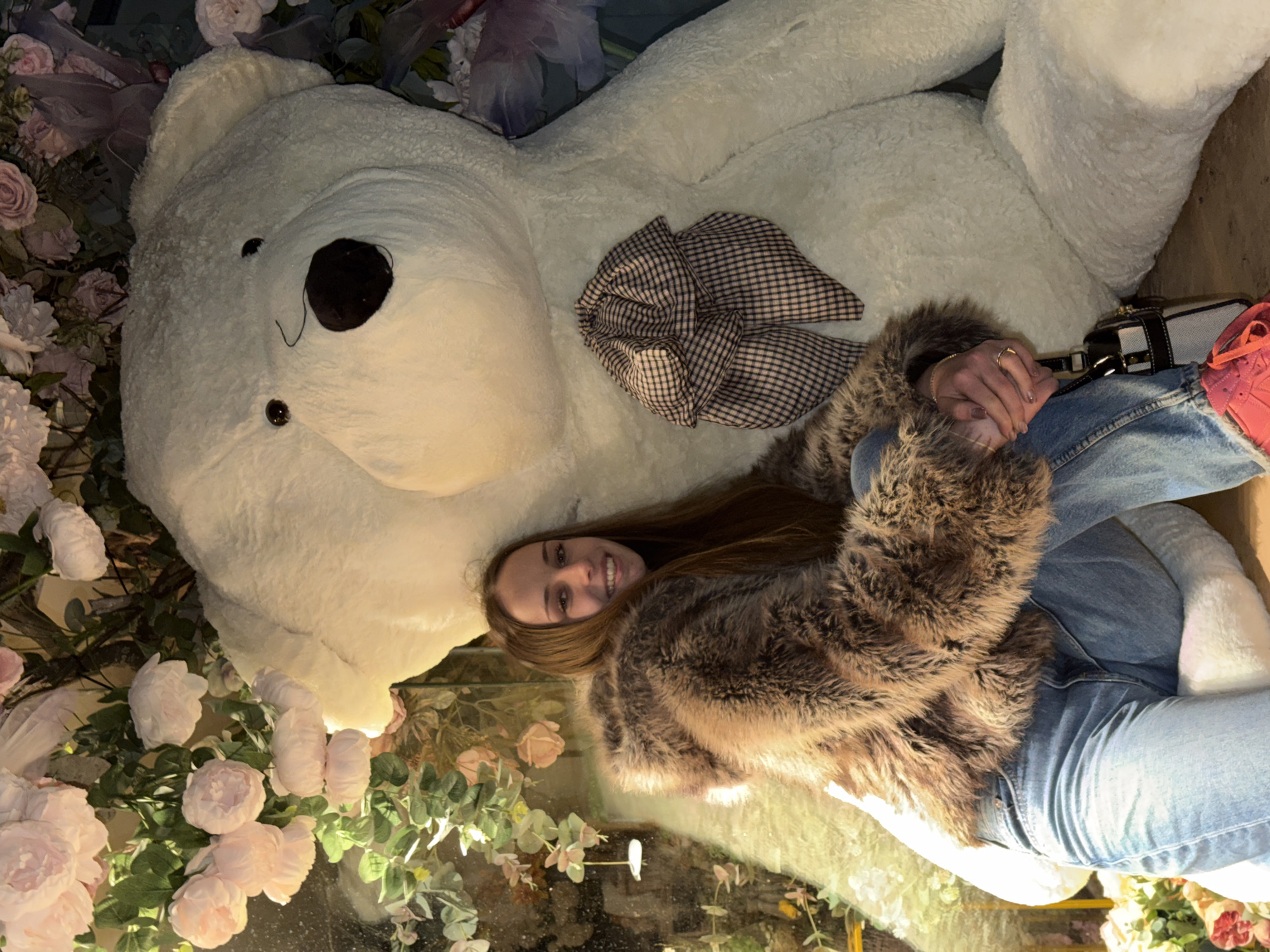 Woman poses with giant teddy bear in floral display