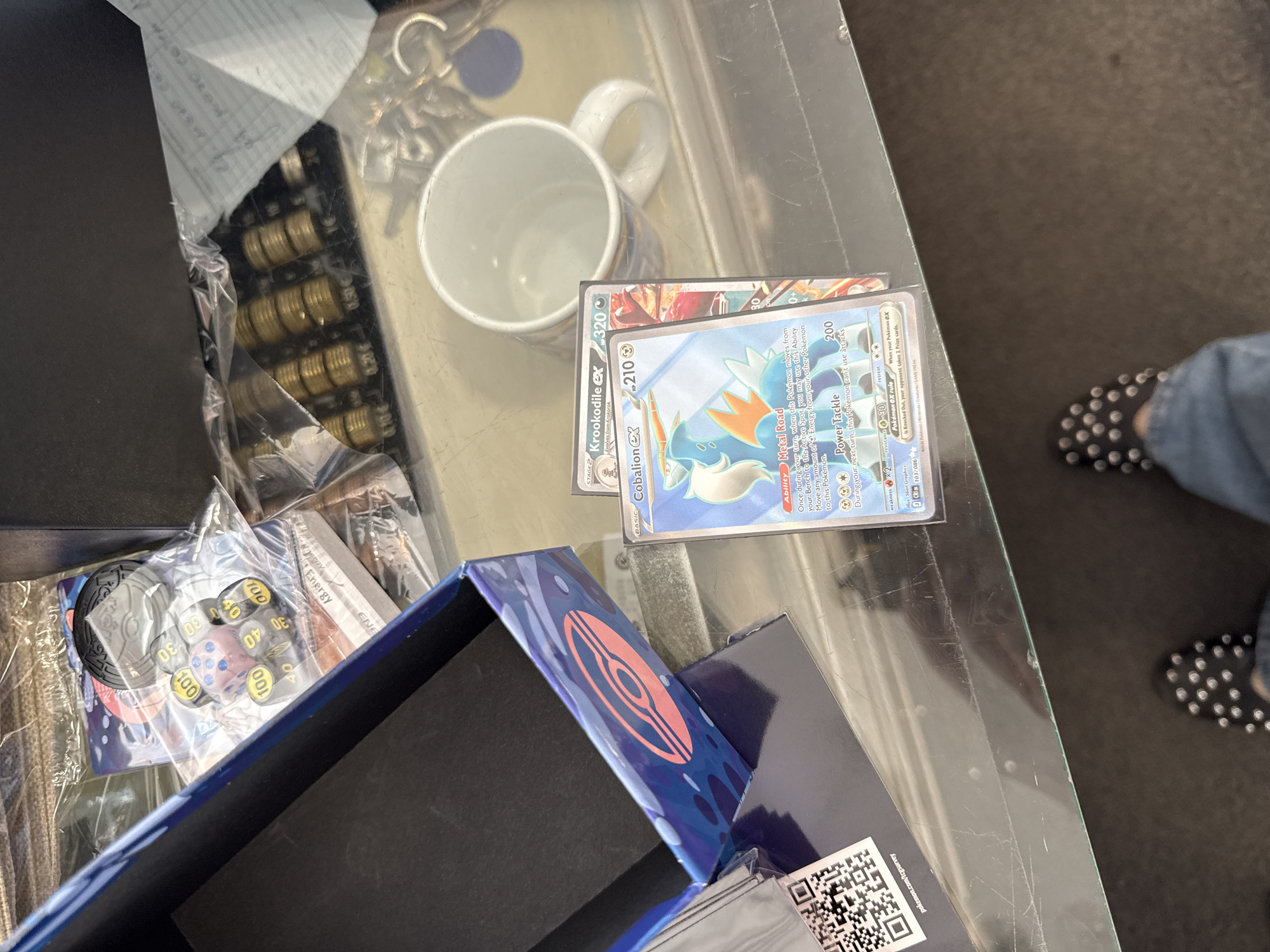 Pokémon cards and Elite Trainer Boxes spread out on a glass table