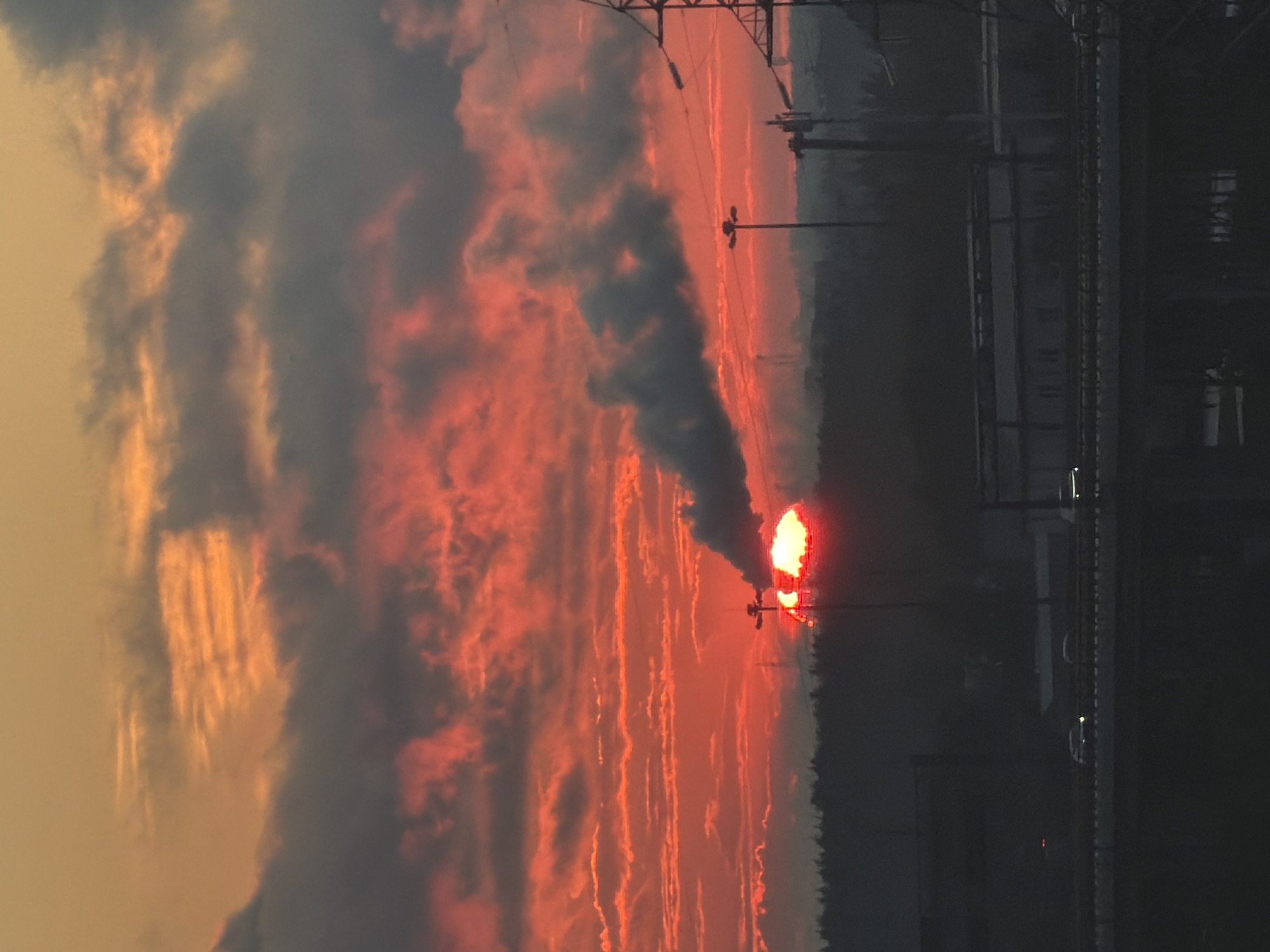 Industrial skyline at sunset, smoke rising against a fiery sky
