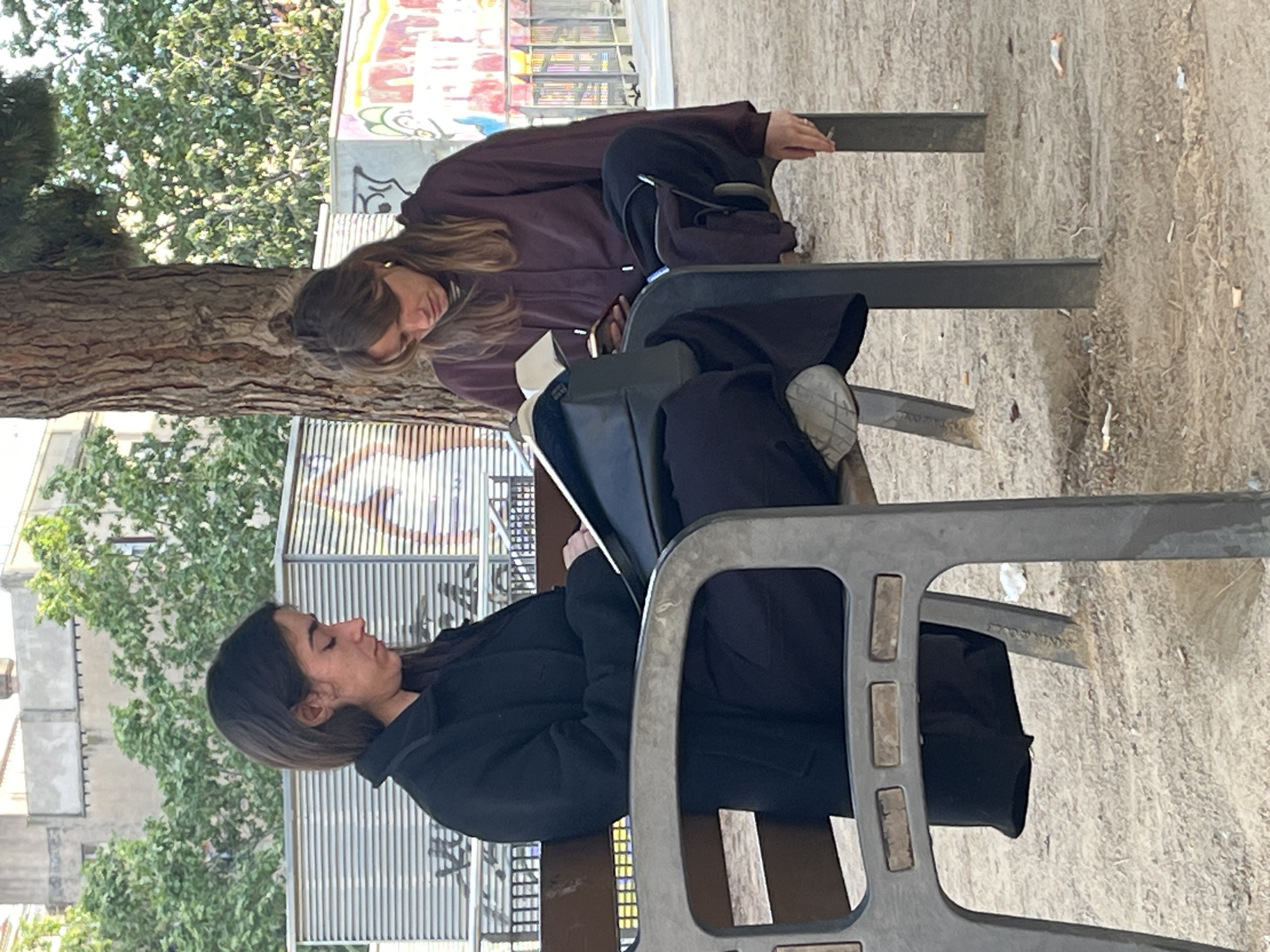 Two women sit on park benches in Barcelona