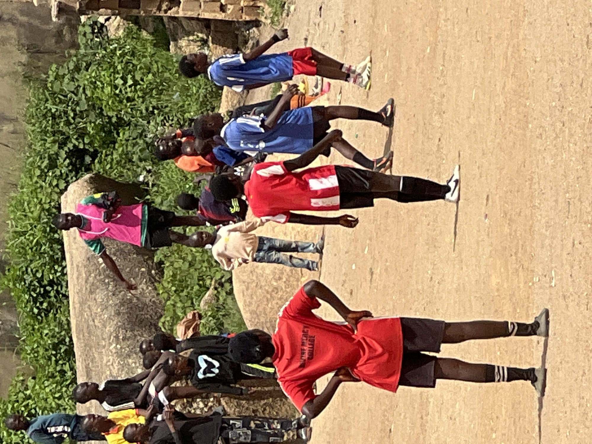 Pickup soccer on a dusty Jos field, midday.