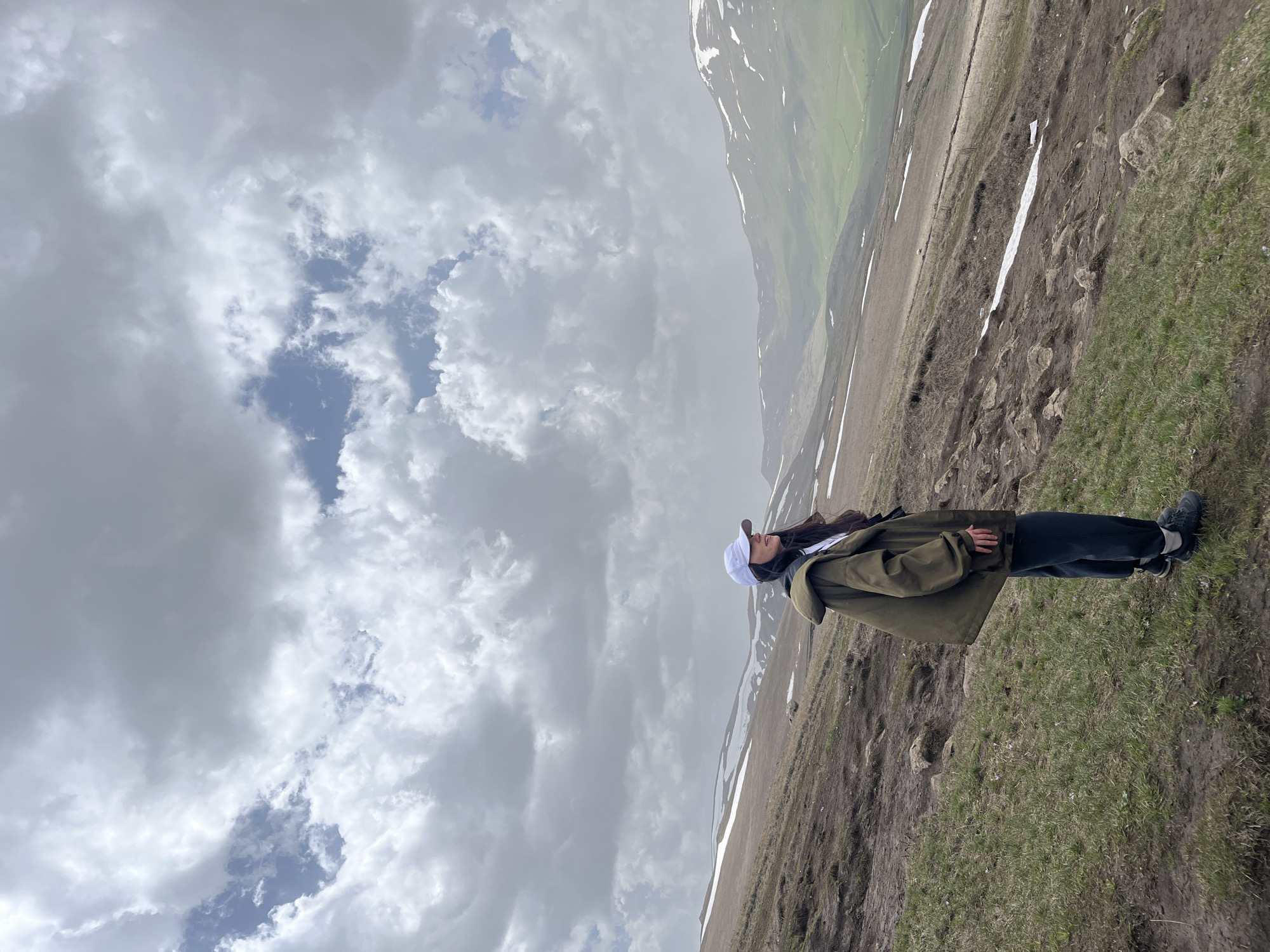 Woman stands on hillside in Hartagyugh, Armenia under cloudy sky