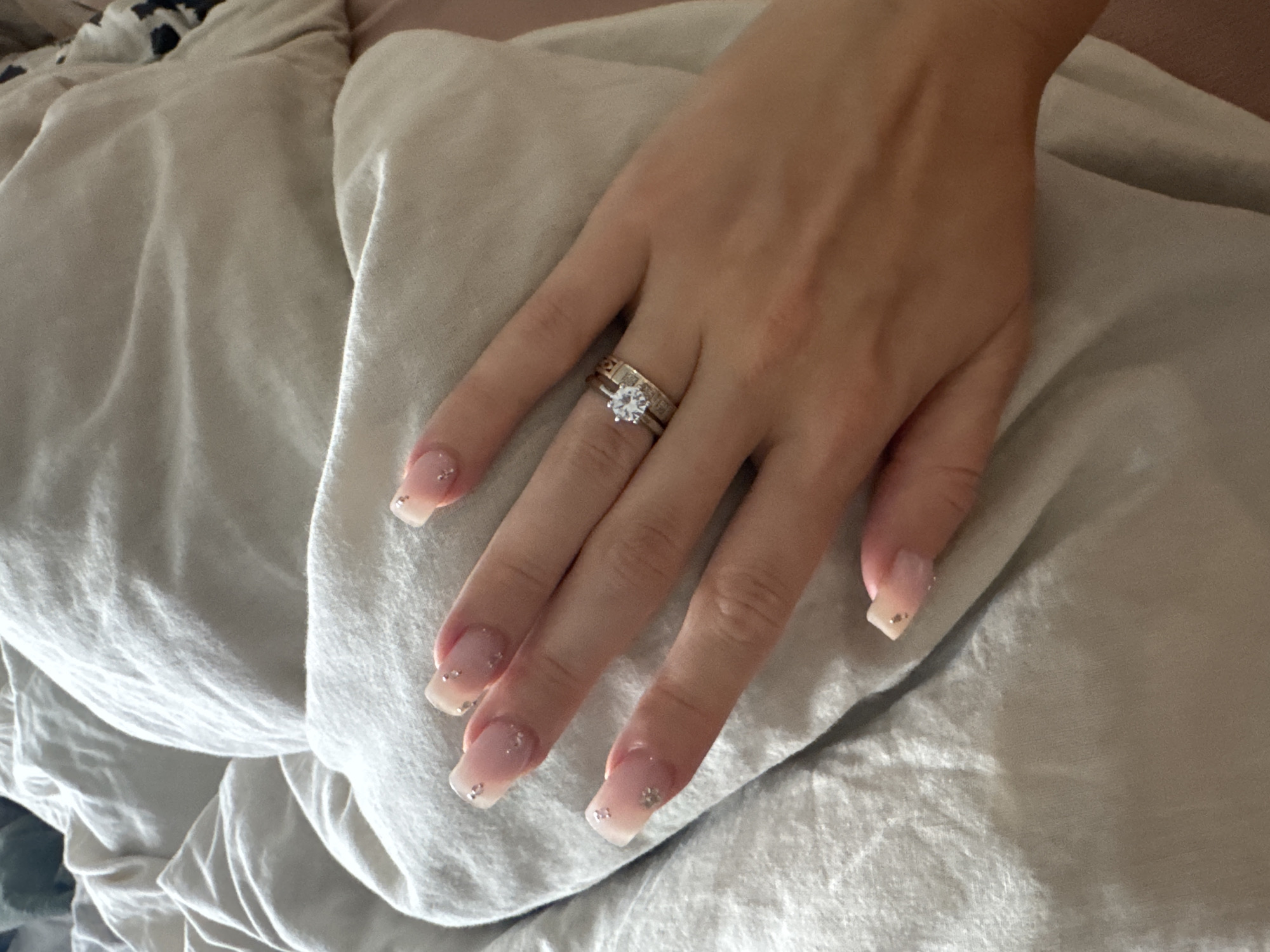Pink acrylic nails with gold glitter resting on textured fabric
