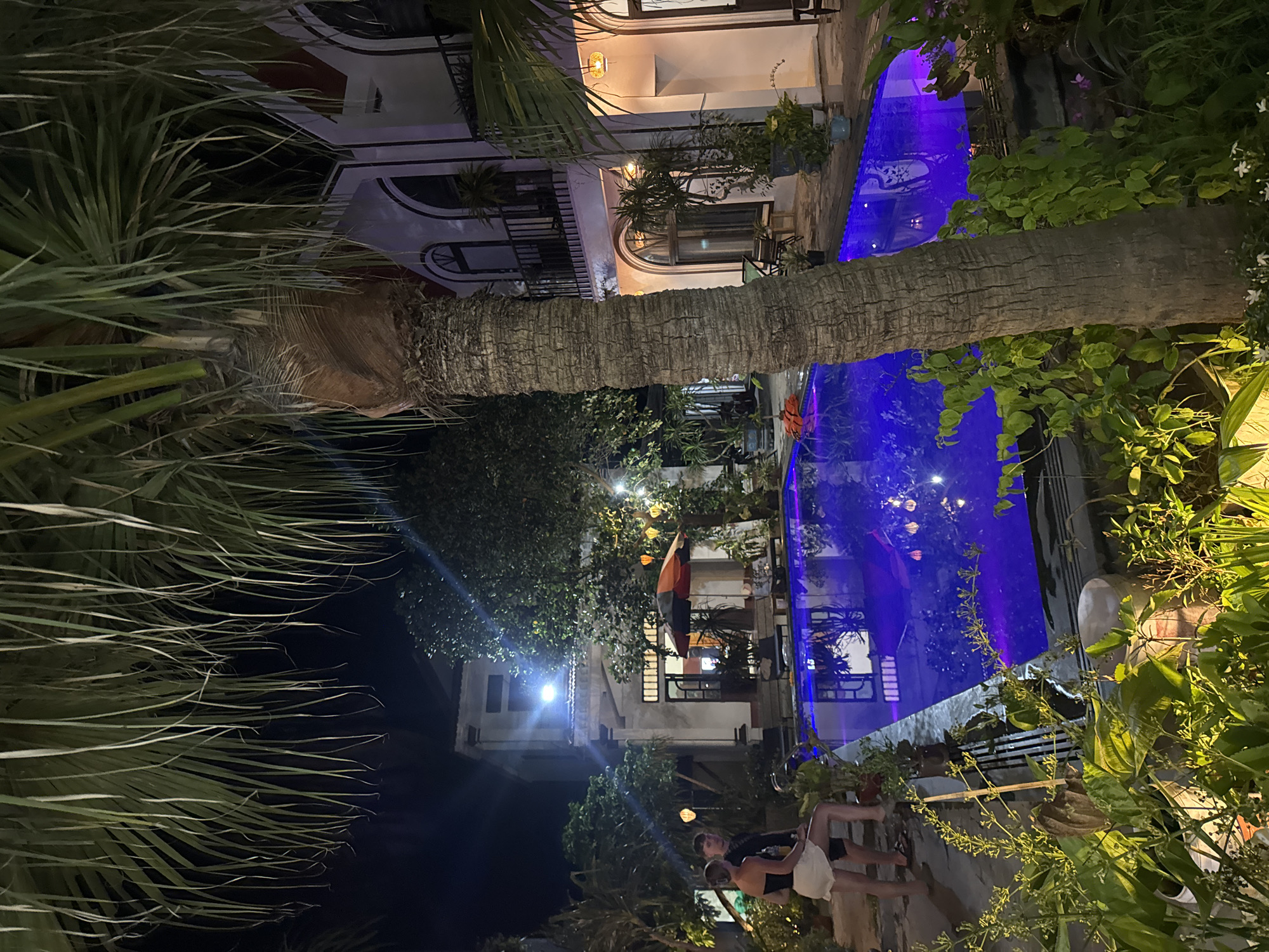 Evening resort gathering with illuminated pool and waterfront boats