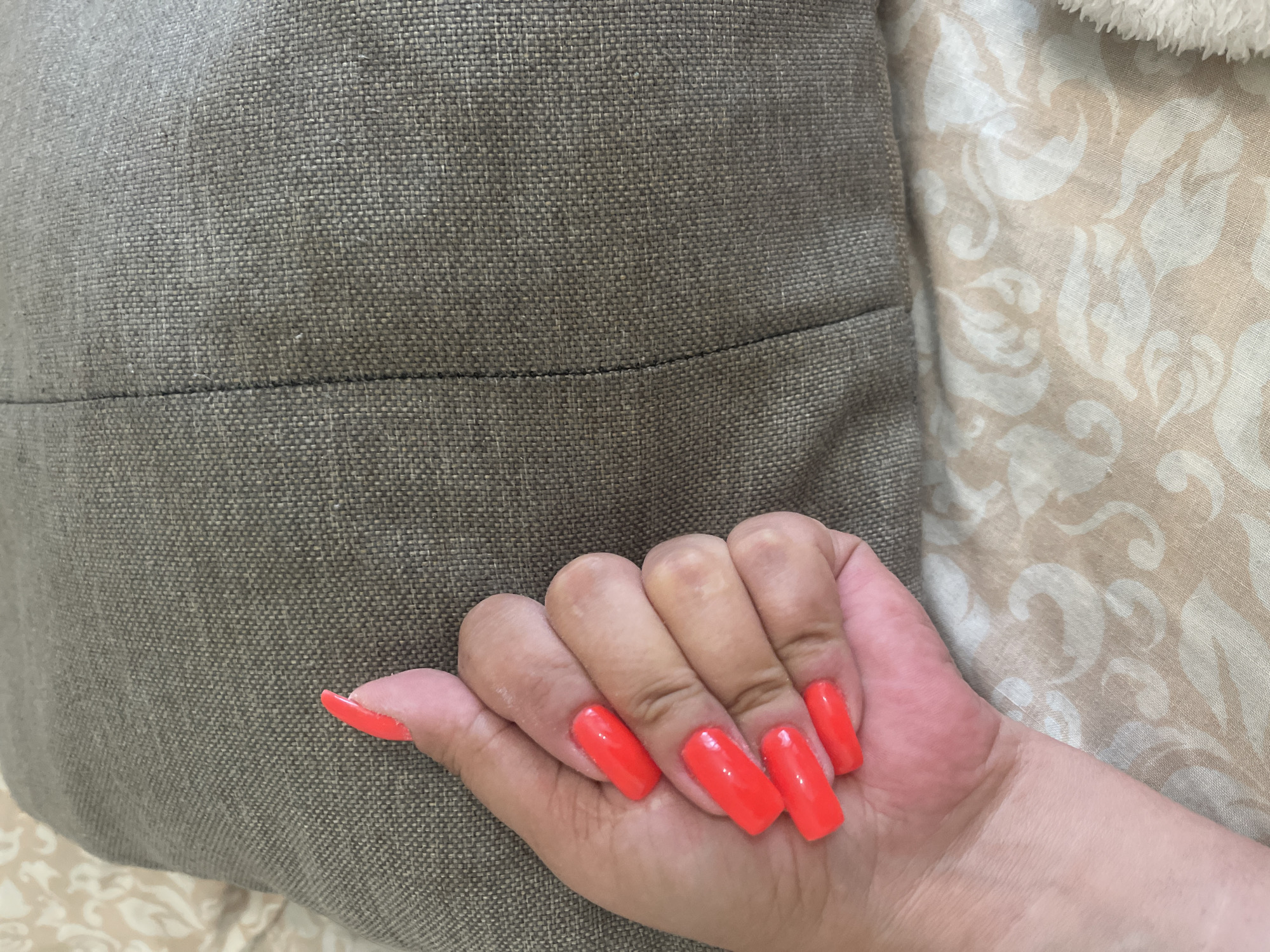 Person displays neon orange square nails on gray fabric