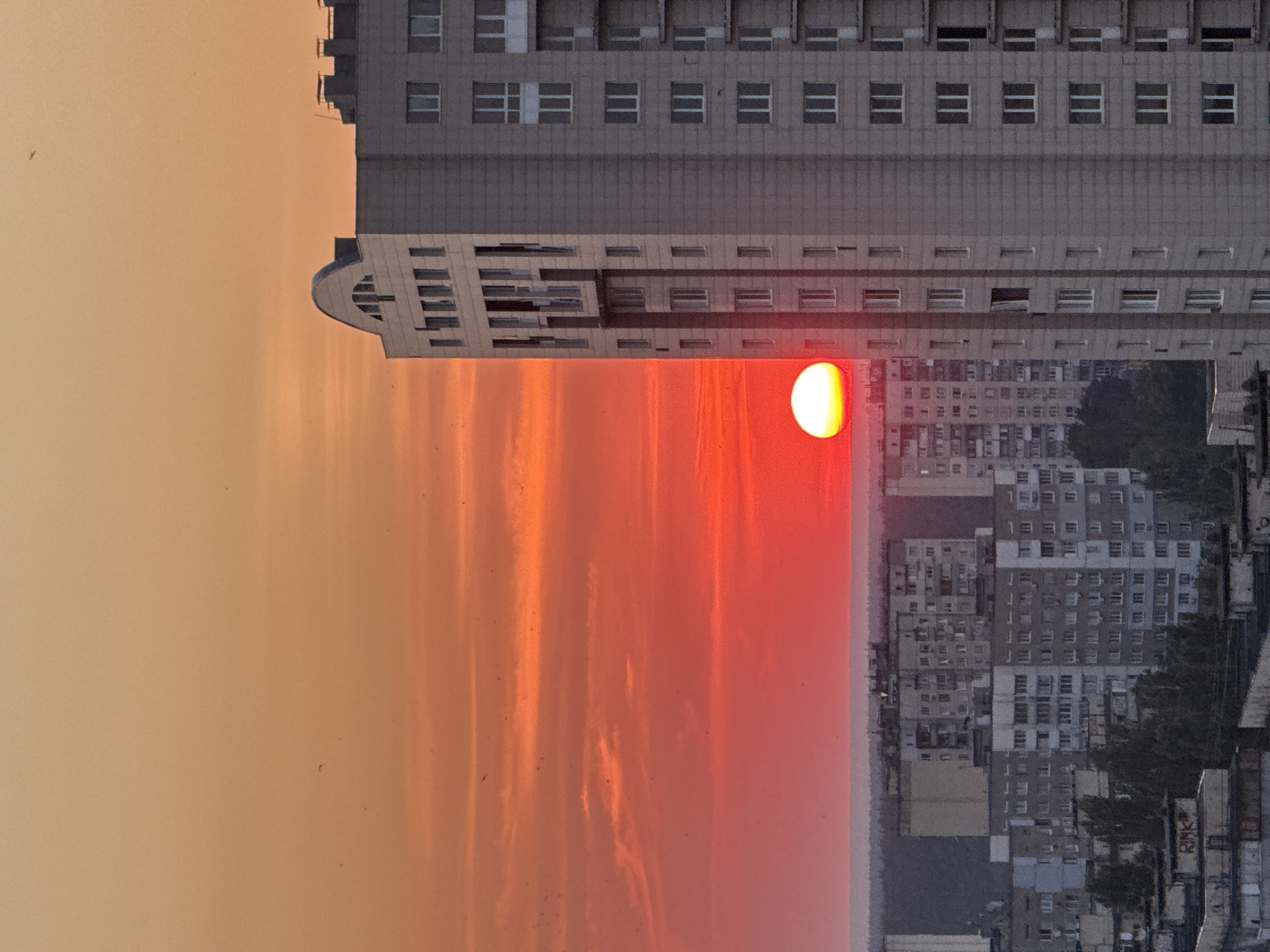City skyline at sunset, sun half-hidden behind apartment tower
