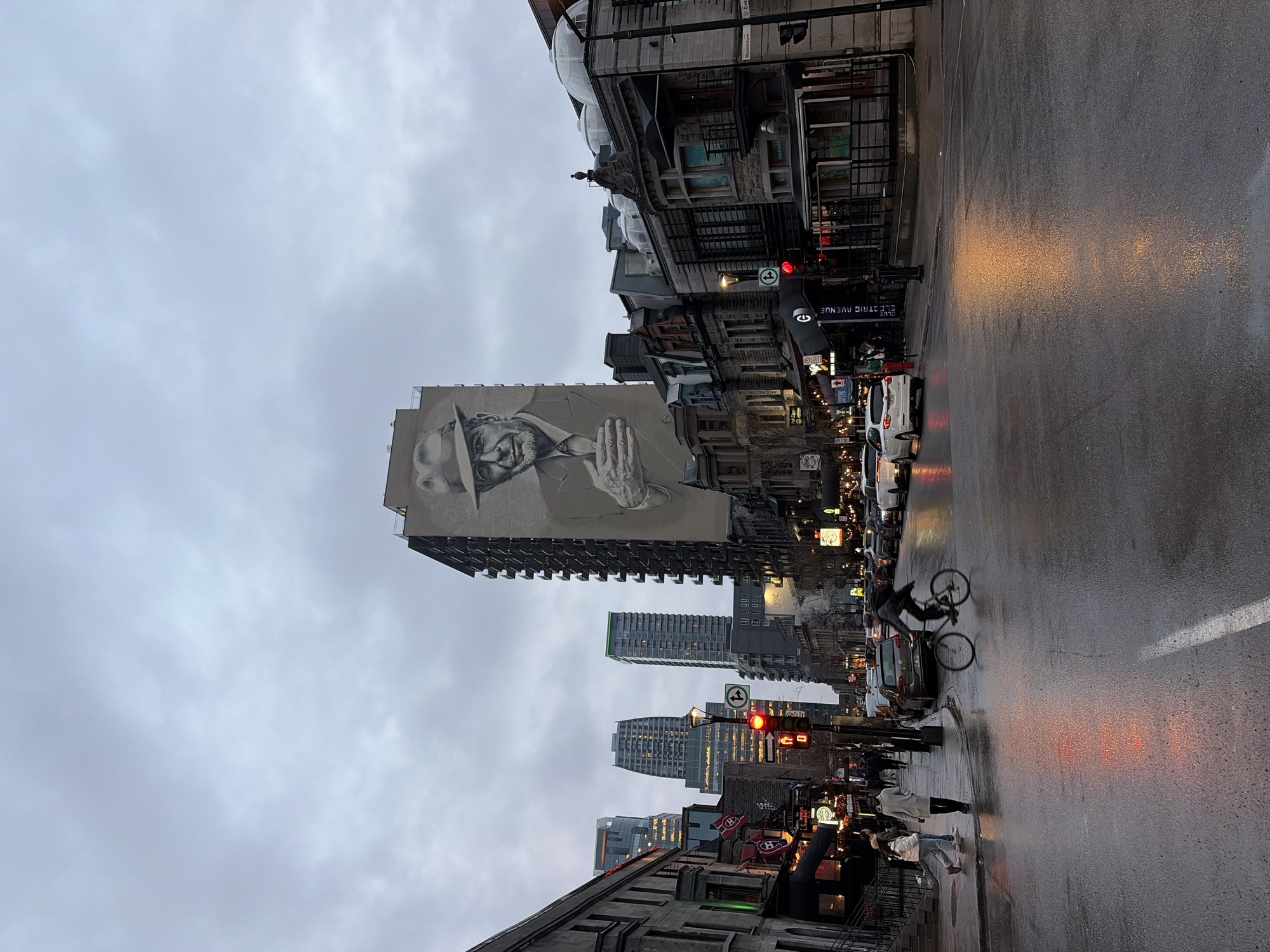 Wet evening street scene observed in Montreal featuring mural