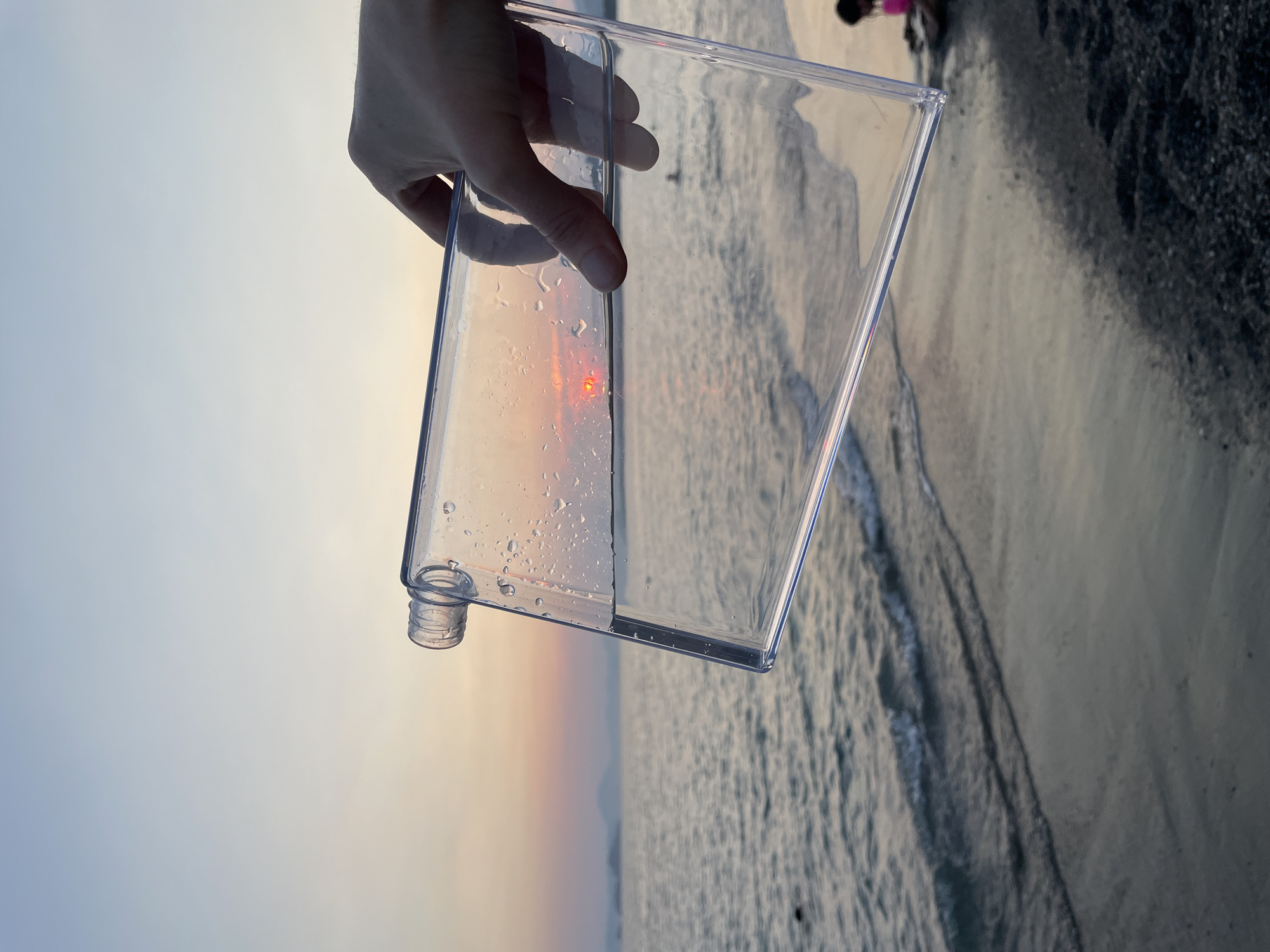 Water bottle held against a beach sunset, sky reflected inside