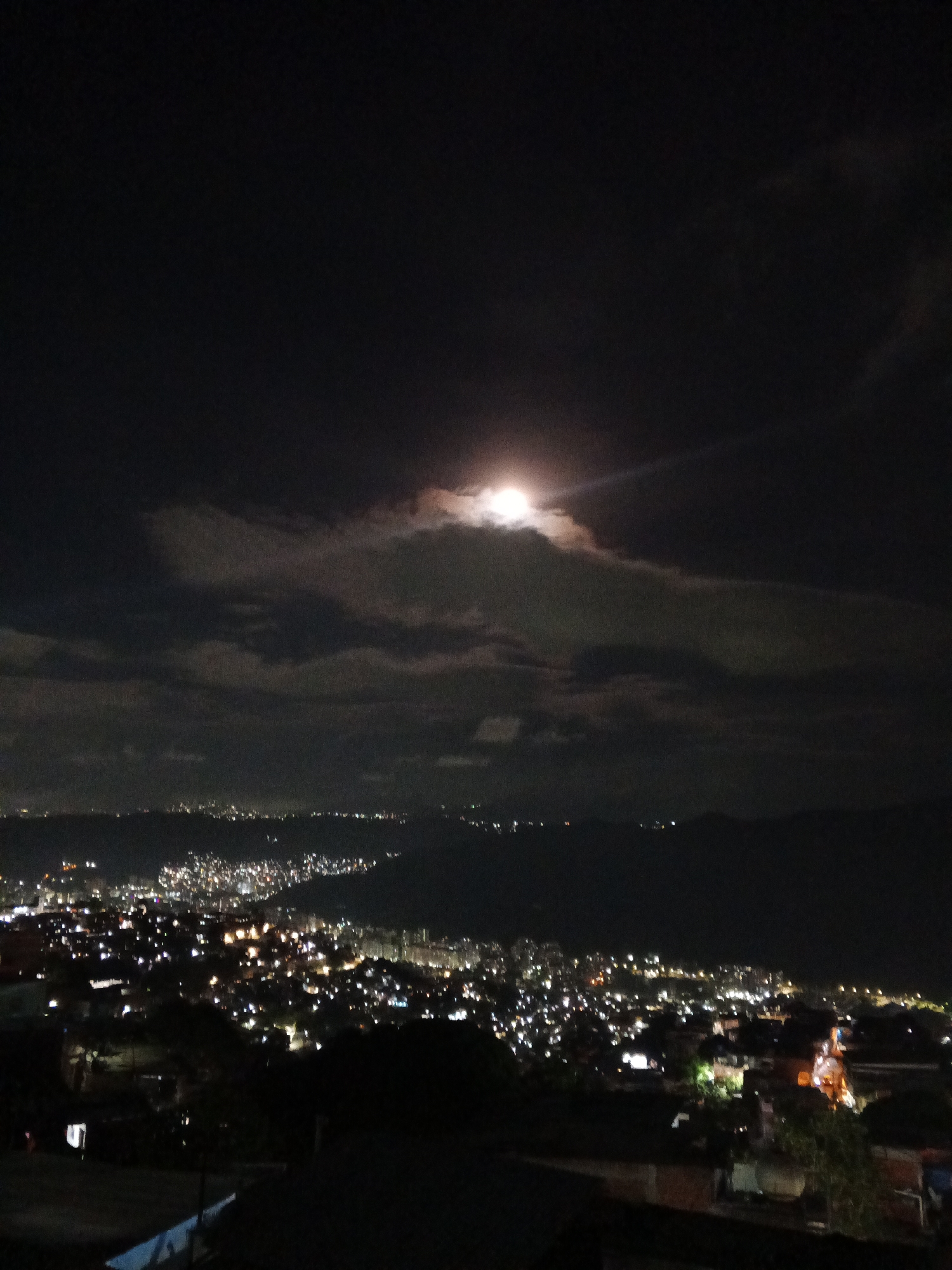 Caracas glows under a clouded full moon from above