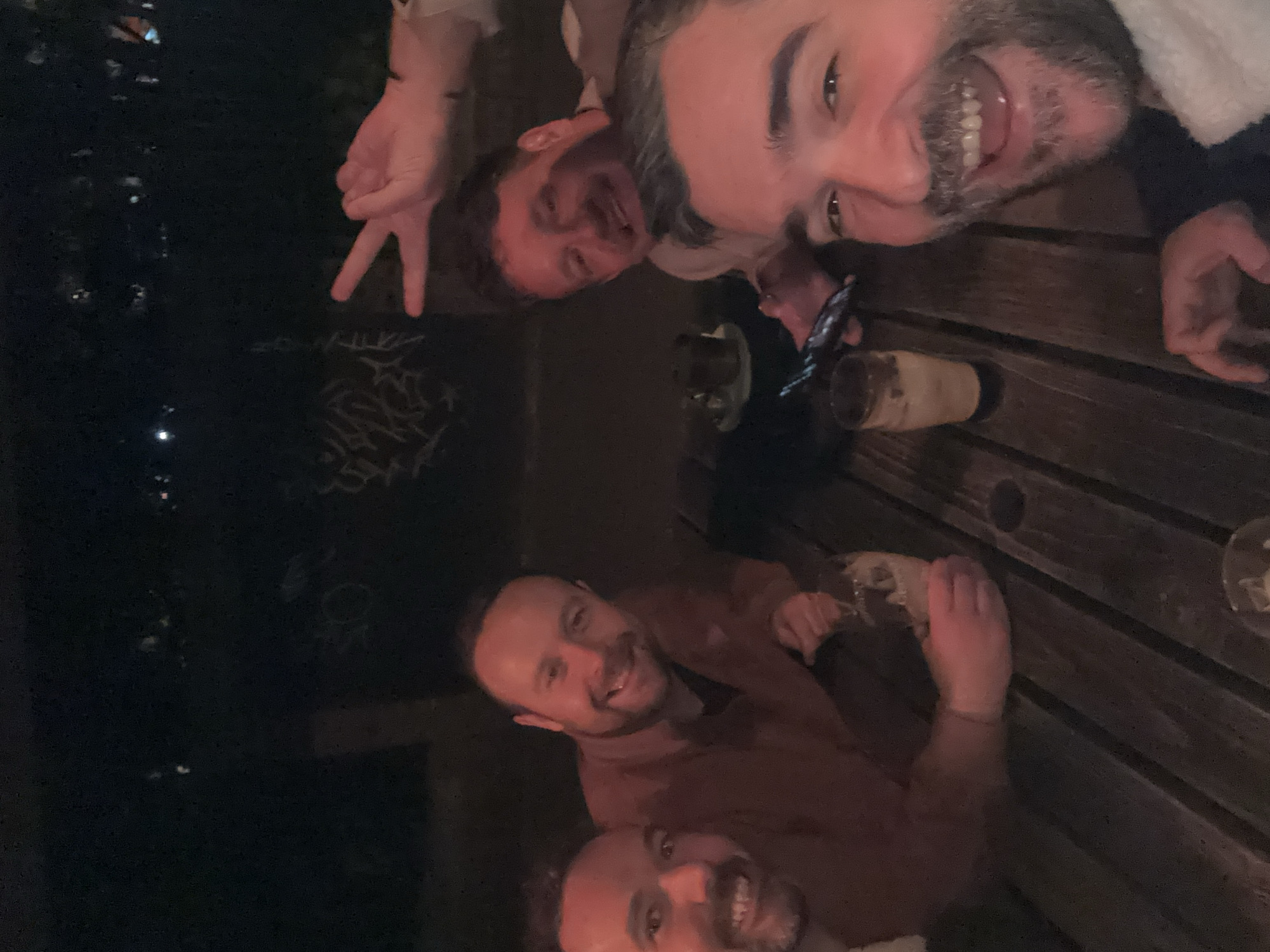 Four men pose for nighttime selfie around outdoor table