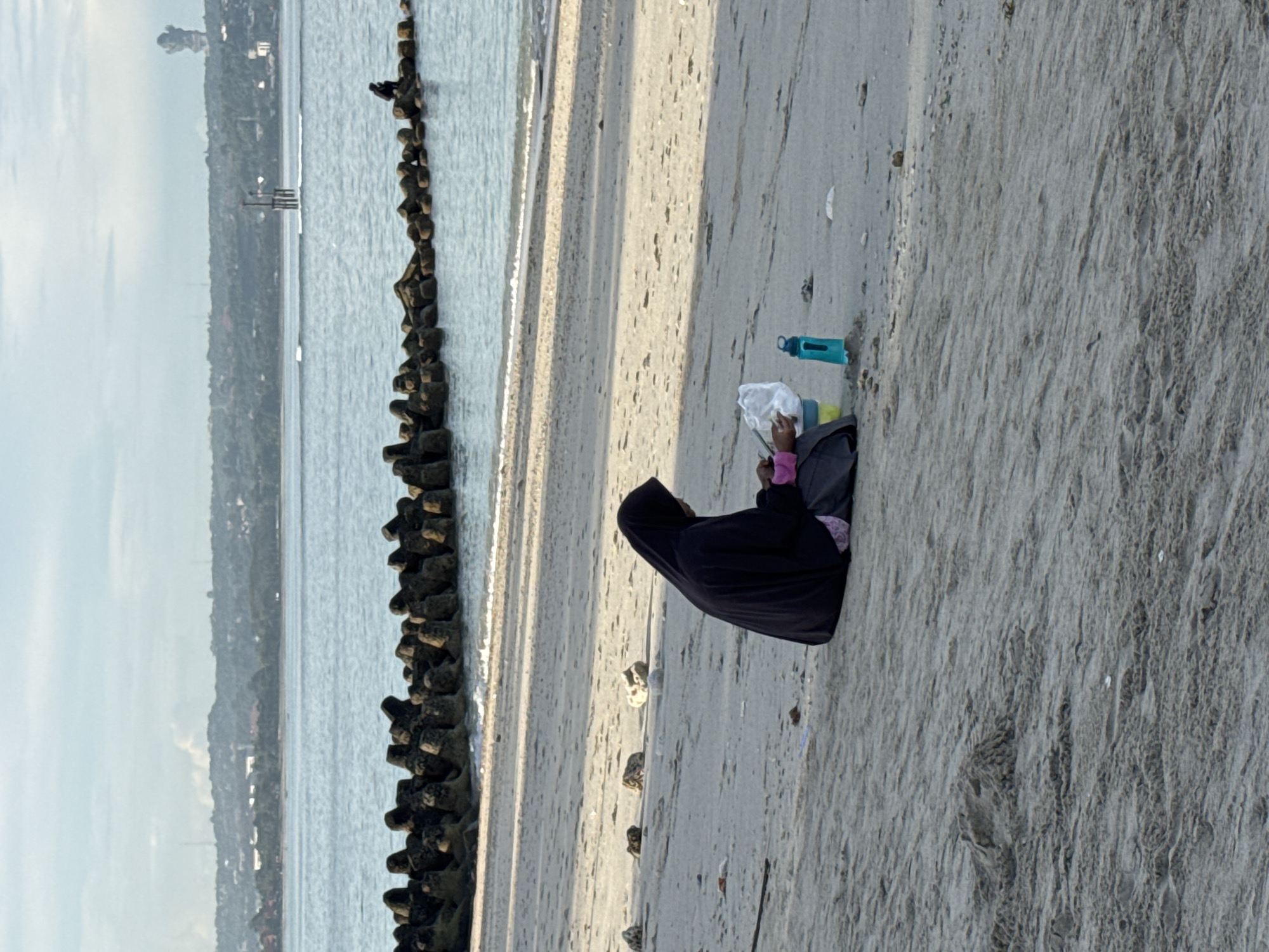 Woman sits on protected Kuta beach holding white object