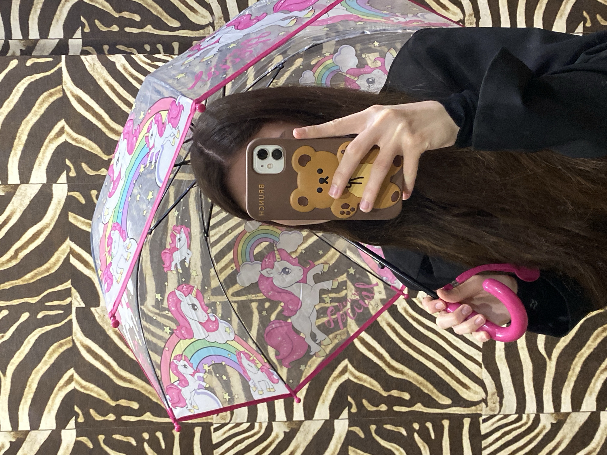 Person takes selfie with unicorn umbrella against zebra backdrop