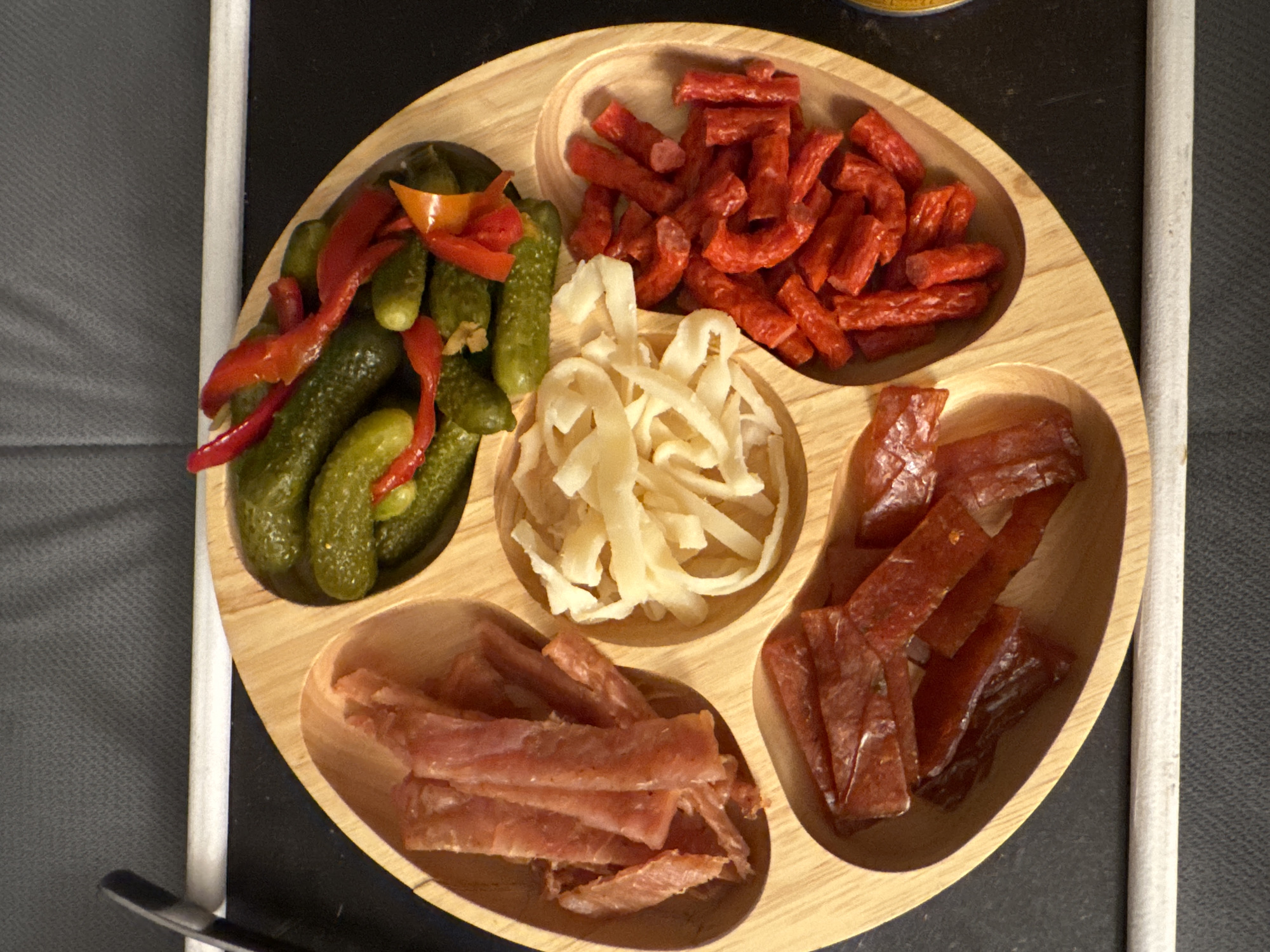 Sectioned wooden food tray with pickles and sausages documented
