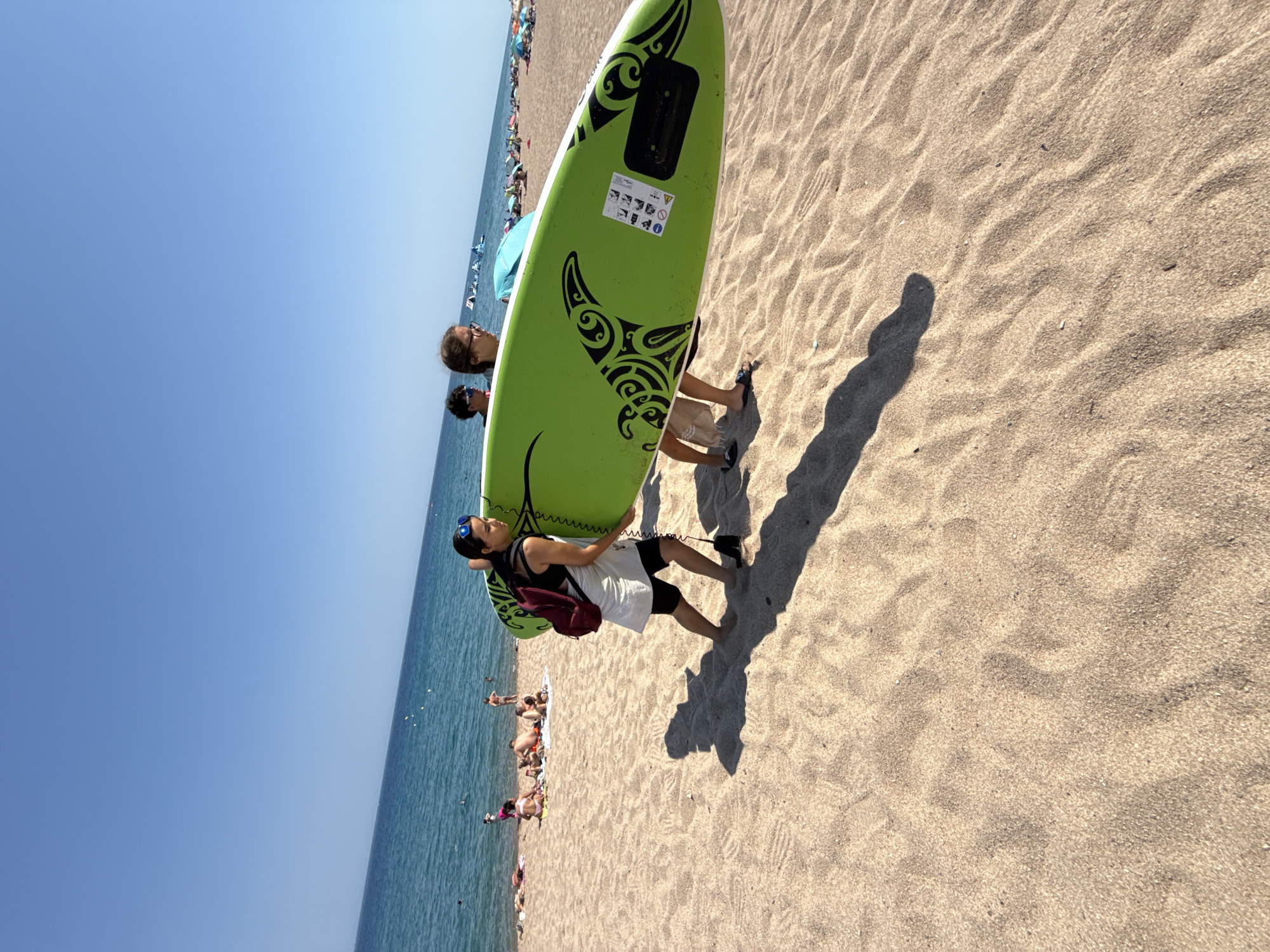Green surfboard heads across a sunny Blanes beach