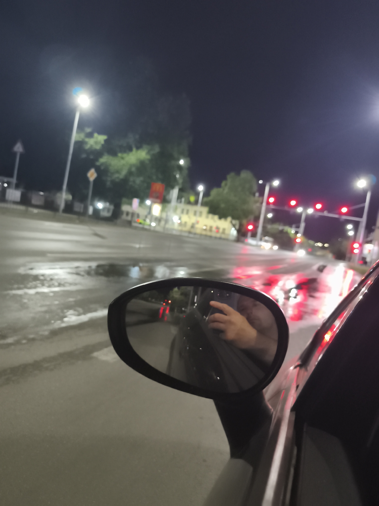 Side mirror reflects a phone-holding hand on a Plovdiv night drive.