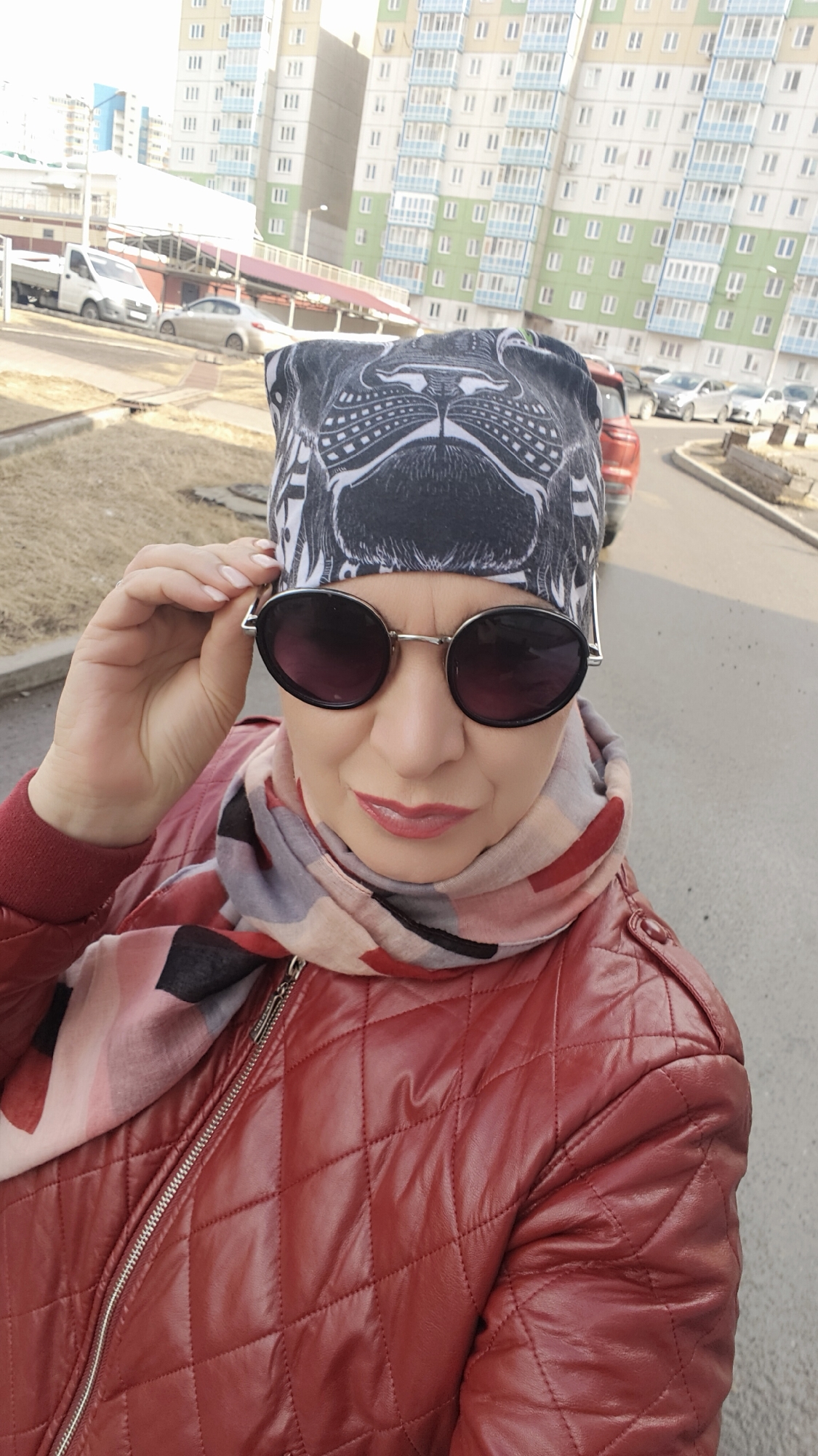 Woman in red jacket takes outdoor selfie, adjusts sunglasses