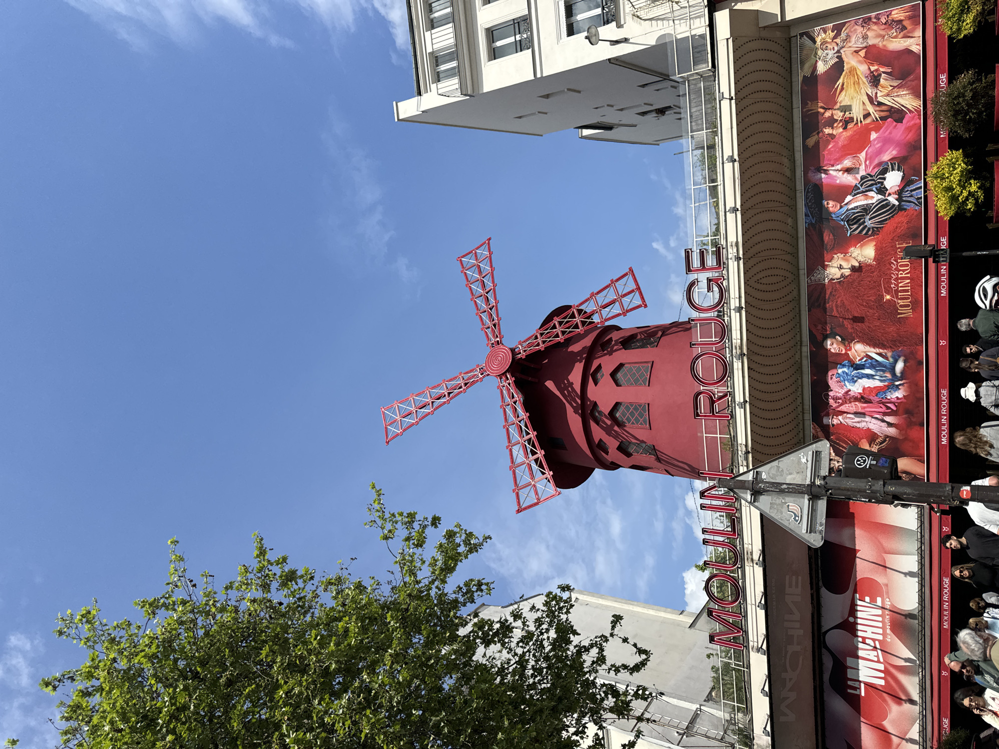 Tourist photographs iconic Moulin Rouge on sunny Paris afternoon