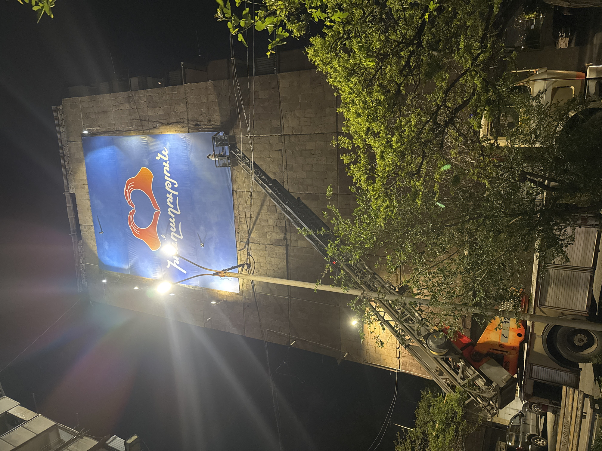 Workers install heart-logo banner on Yerevan building at night
