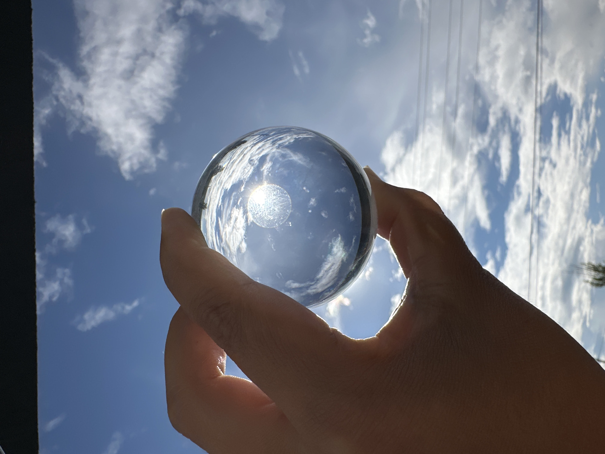 Person photographed with crystal ball against cloudy sky