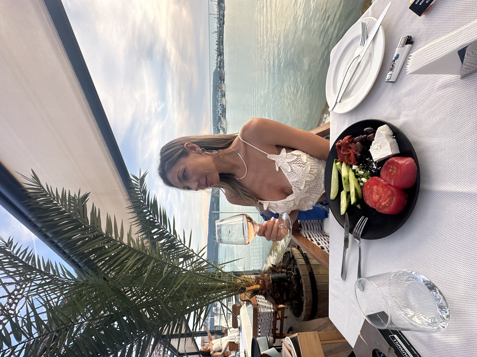 Woman dines waterside with rosé wine and tomatoes