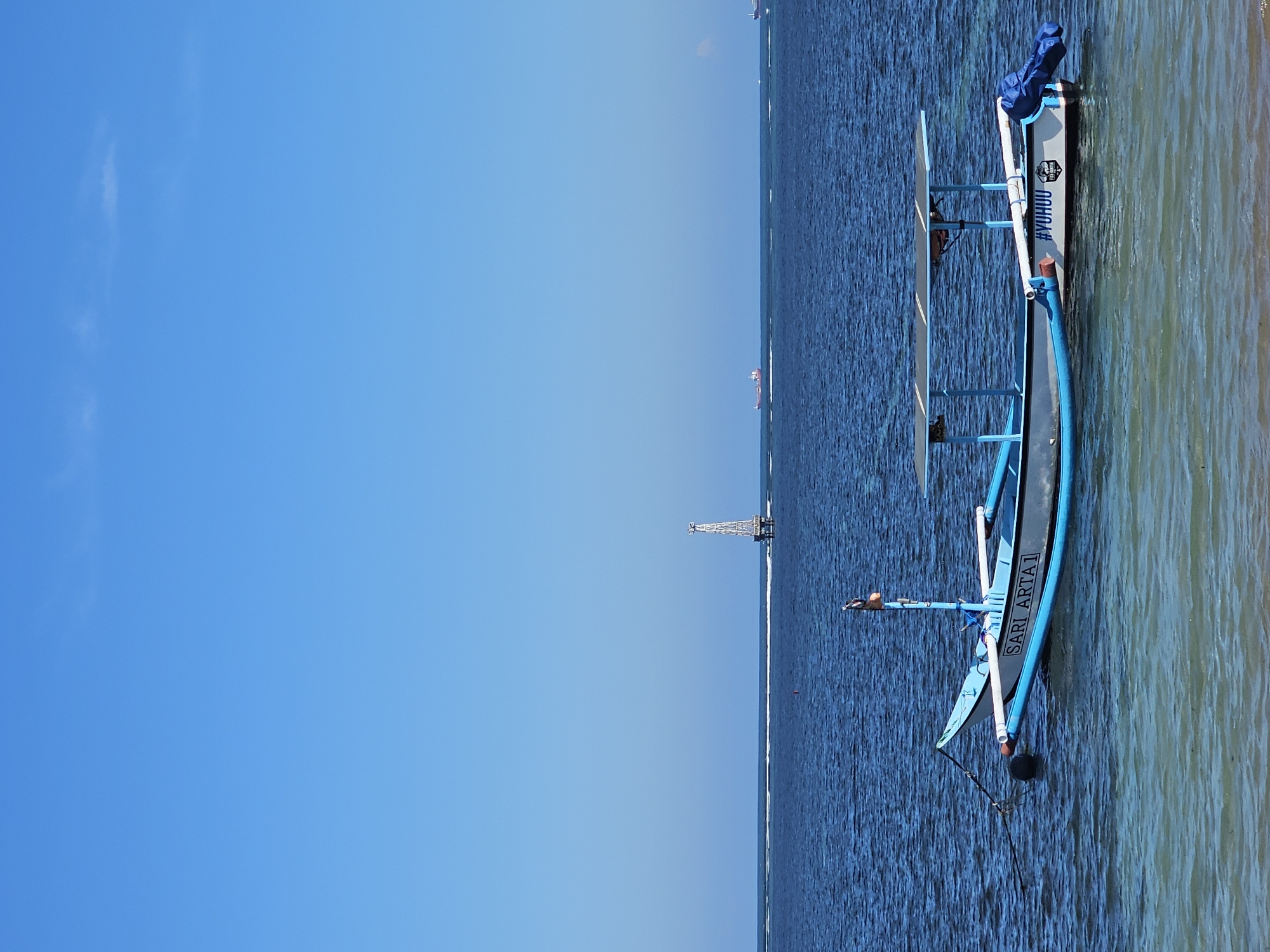 Quiet morning at Sanur Beach, boats, shade trees, and calm water.