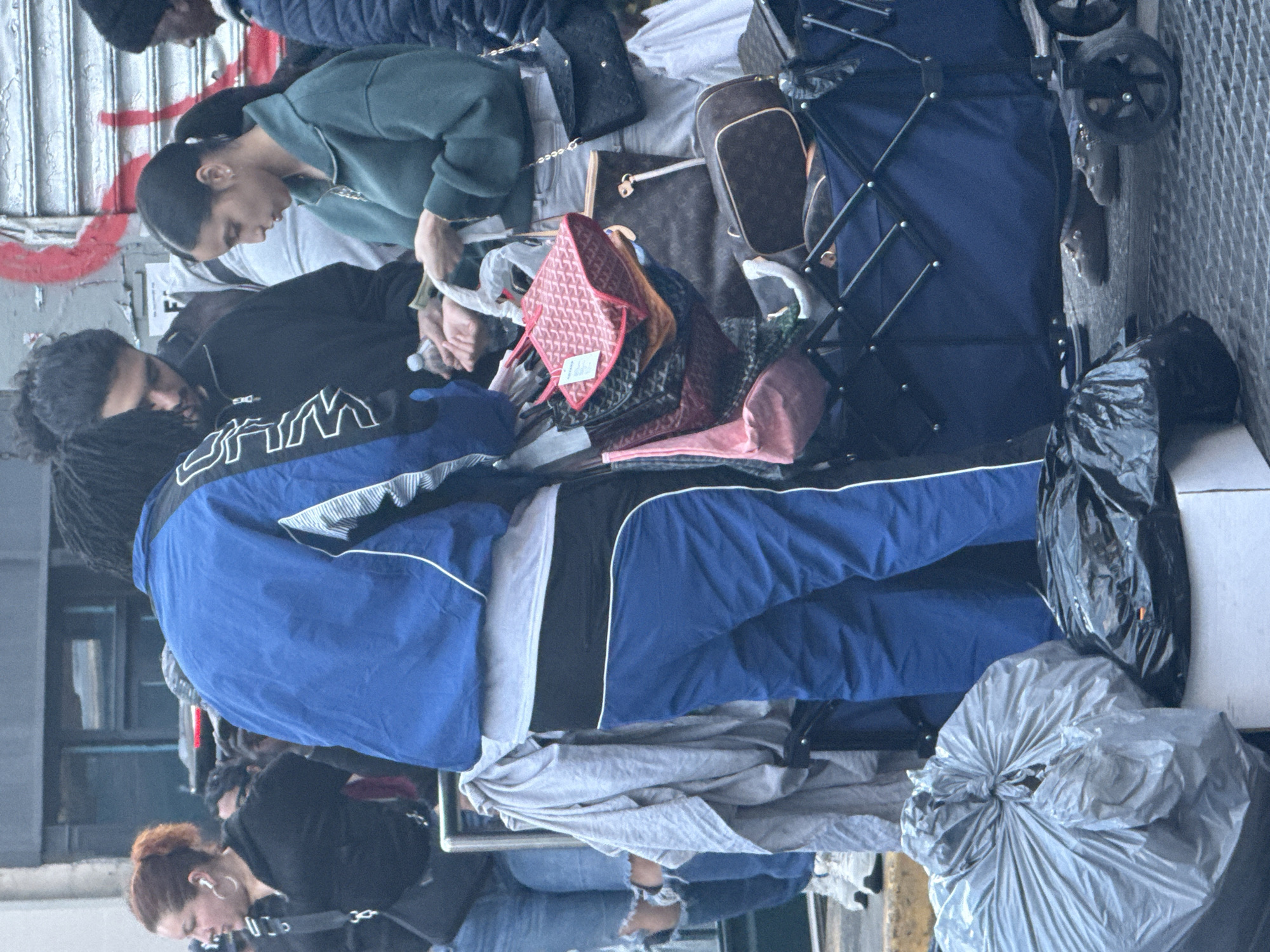People queue on NYC sidewalk with belongings near shuttered storefront