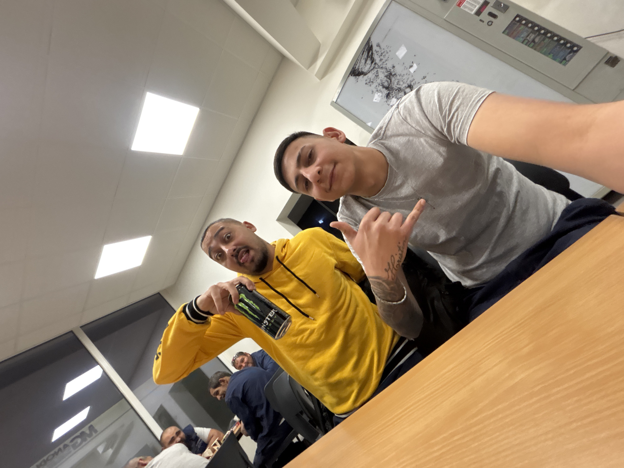Two men pose for selfie indoors with energy drink